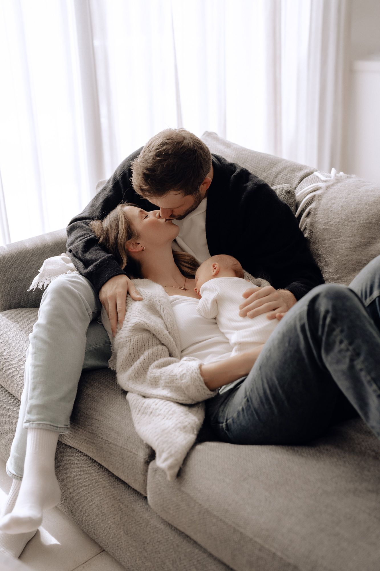 Intimate couple in cozy winter attire sharing a tender moment while relaxing together on a grey sofa.
