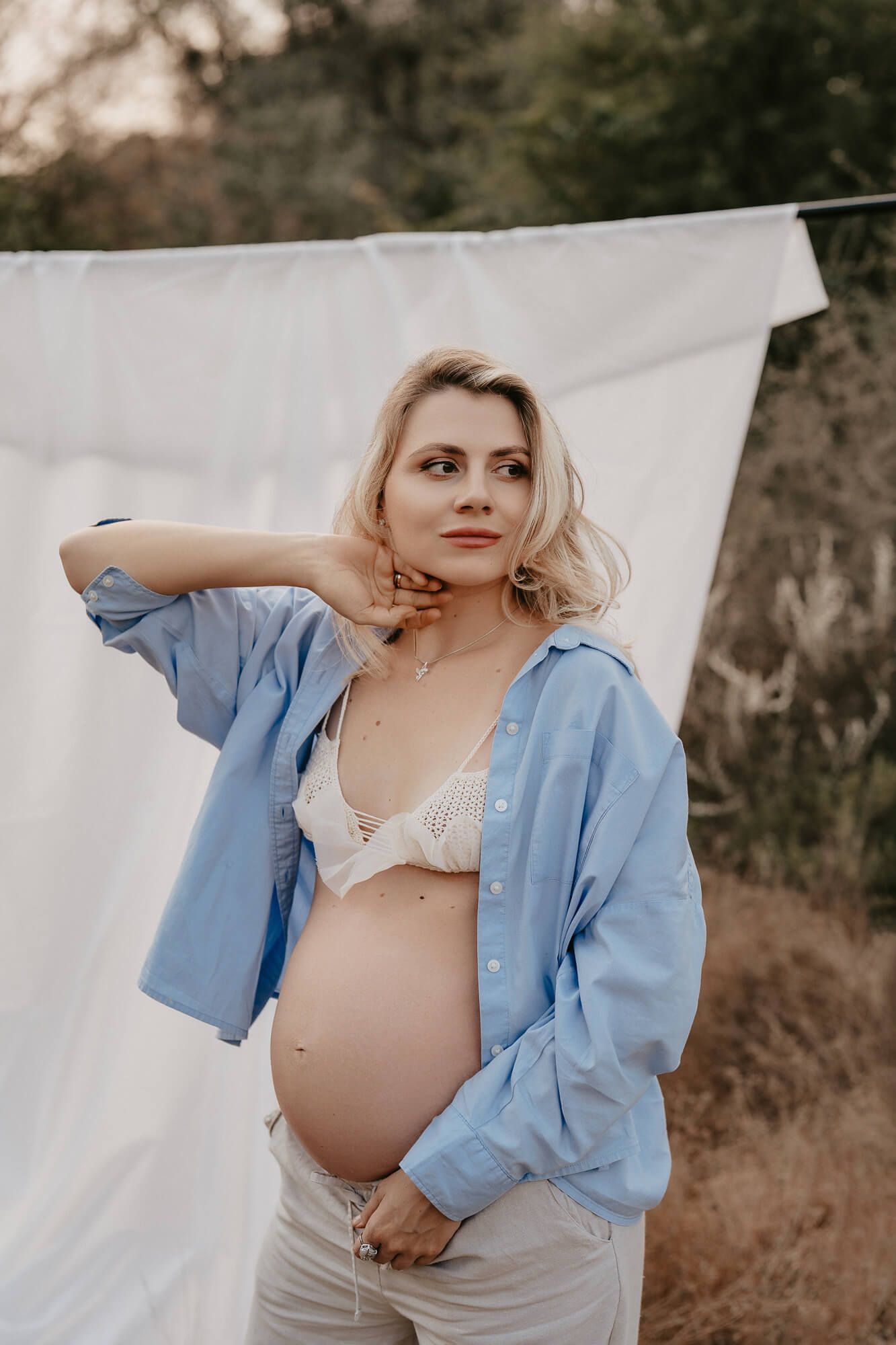 Maternity photoshoot outdoors with pregnant woman wearing blue button down shirt and white bra.