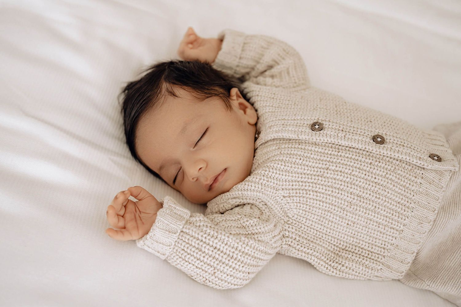 Baby sleeping peacefully in cream knit sweater during newborn photoshoot.
