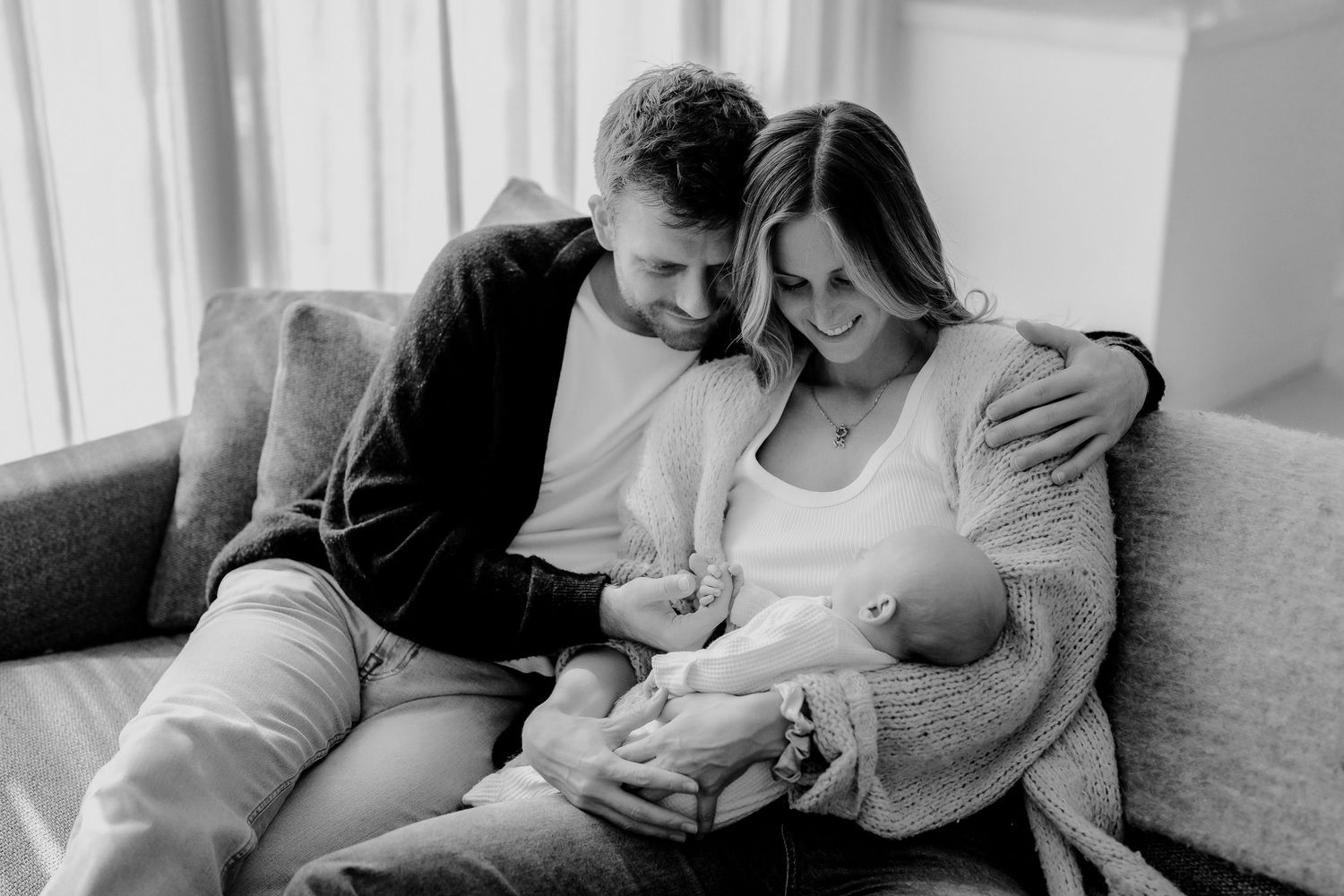 Black and white photo of a couple on couch tenderly holding their newborn baby.