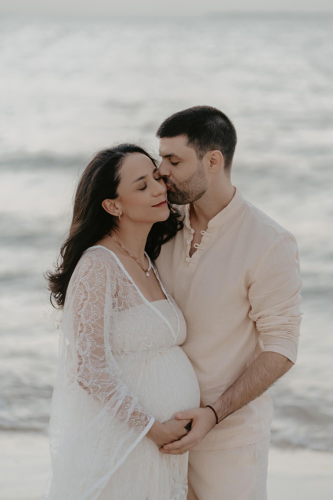 A romantic couple embraces on a misty beach in soft neutral tones during an intimate photoshoot.