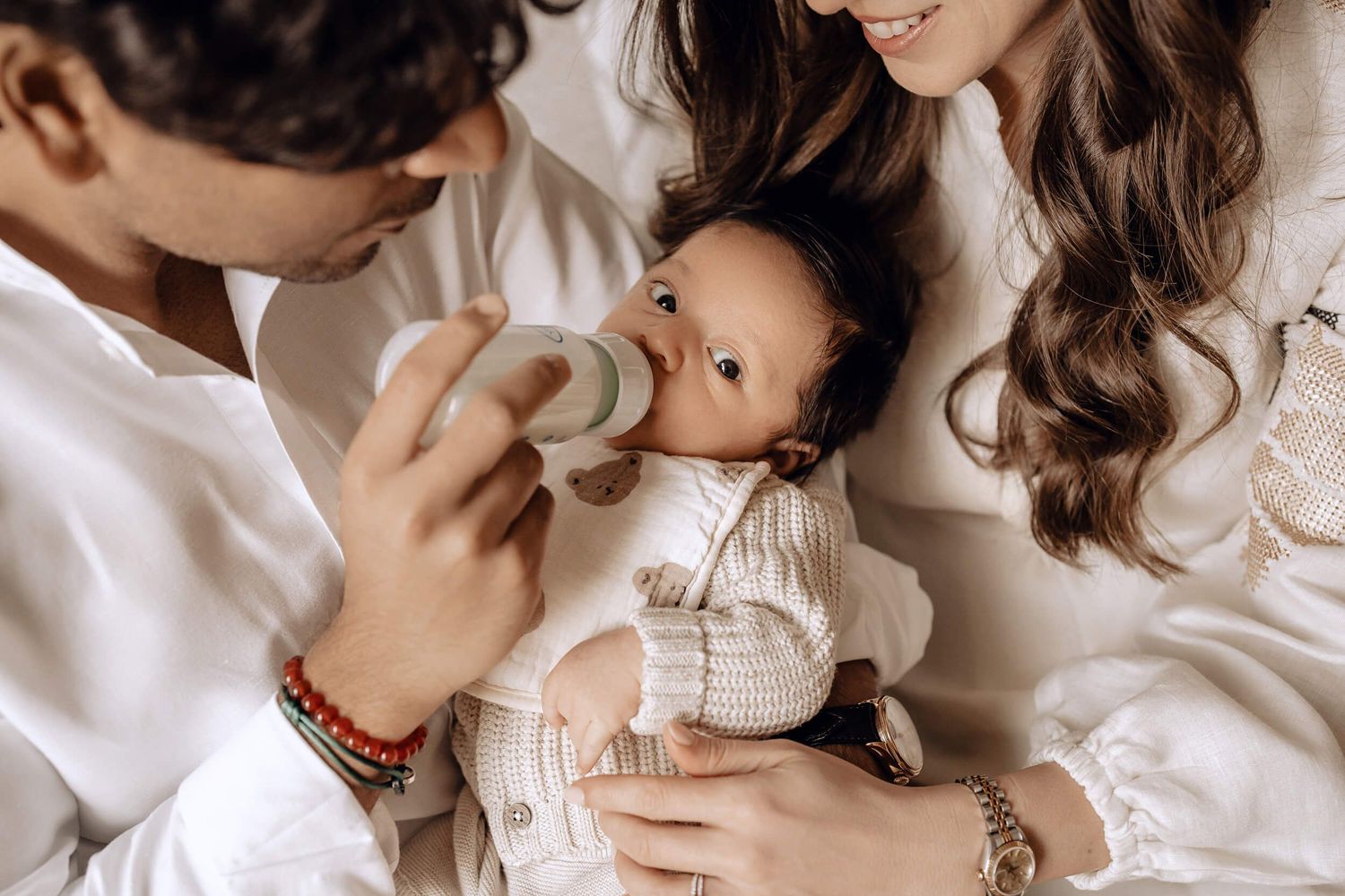 A tender moment of bottle feeding a baby wearing a white sweater while being cradled in loving arms.