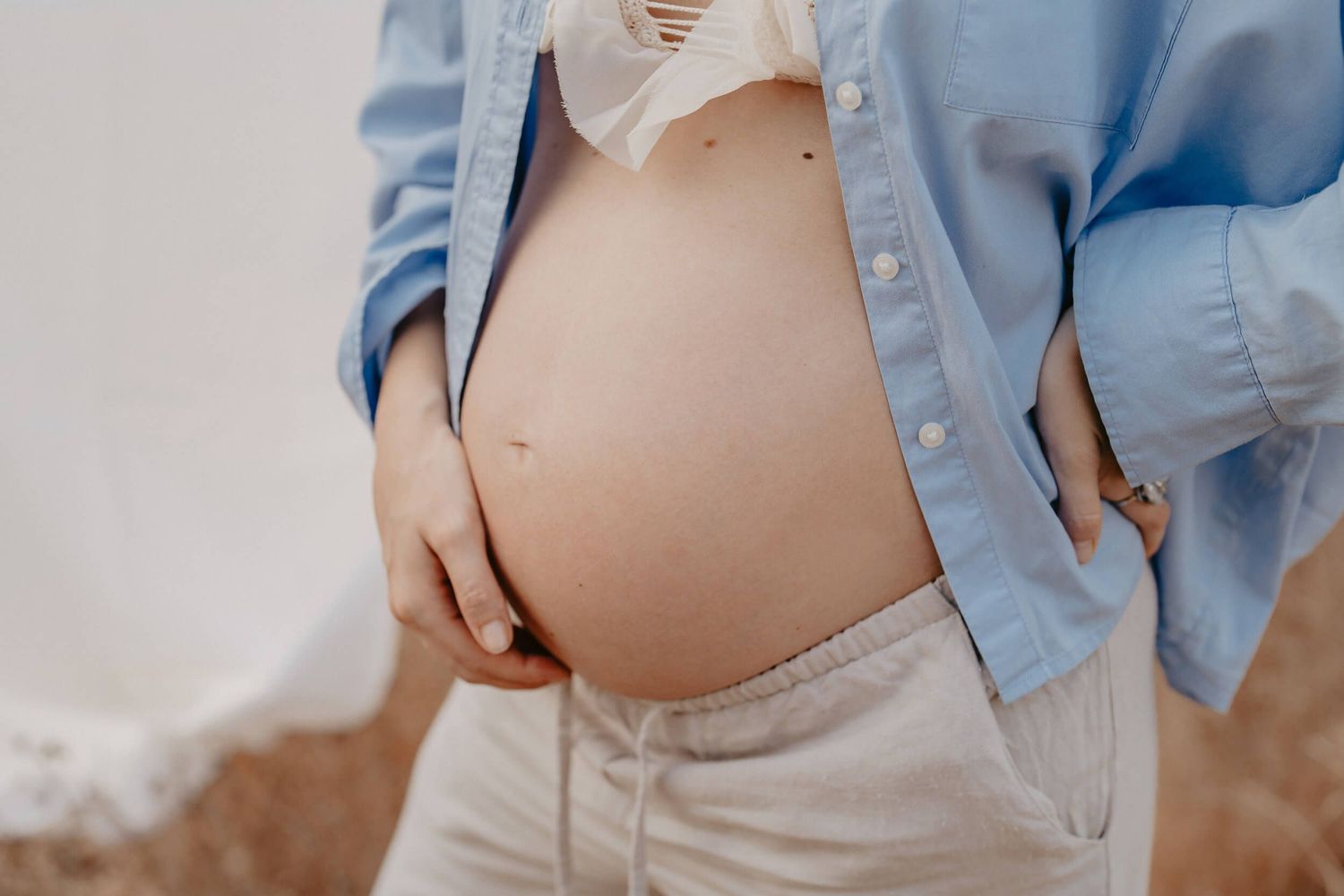 Close up shot of a pregnant belly with a light blue denim jacket framing the bump.