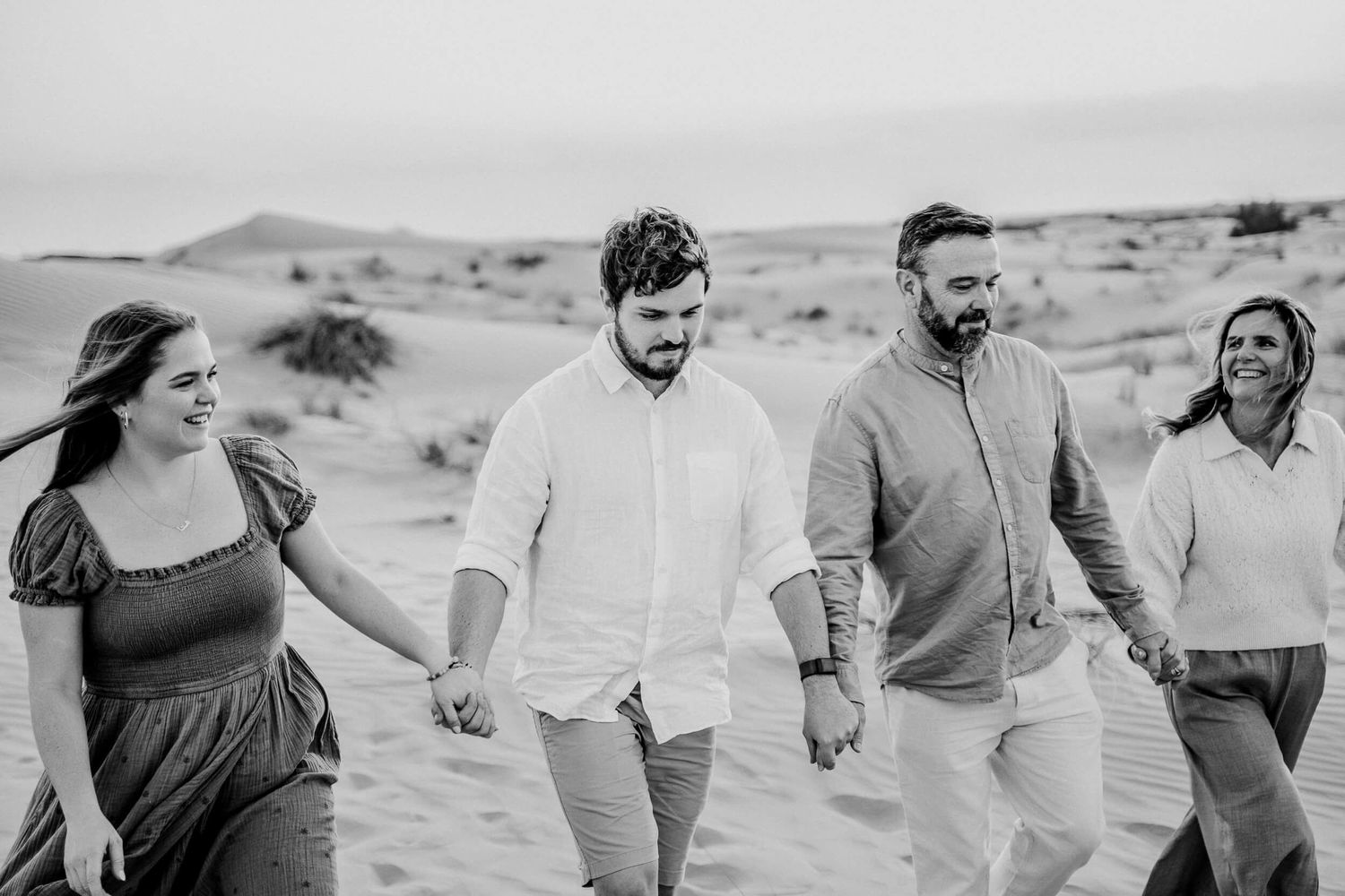 Black and white photo of group walking together through desert landscape holding hands.