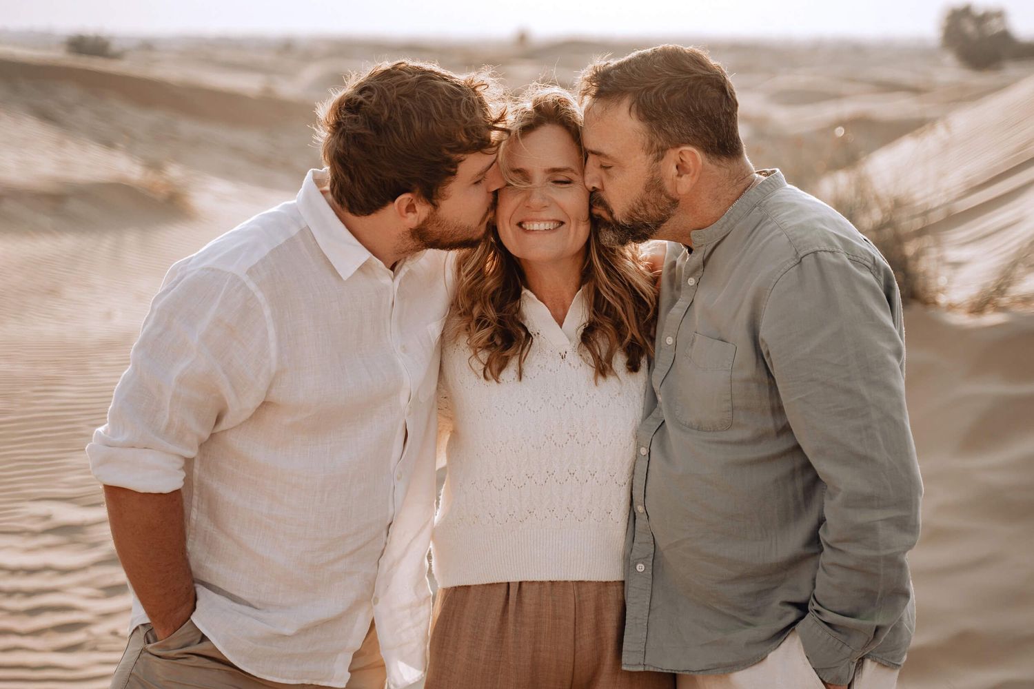 Three people share tender moments and laughter while taking photos in a desert environment.