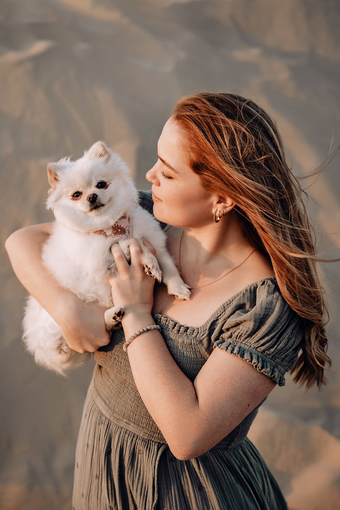 Portrait of person in gray dress holding small white dog against desert backdrop.