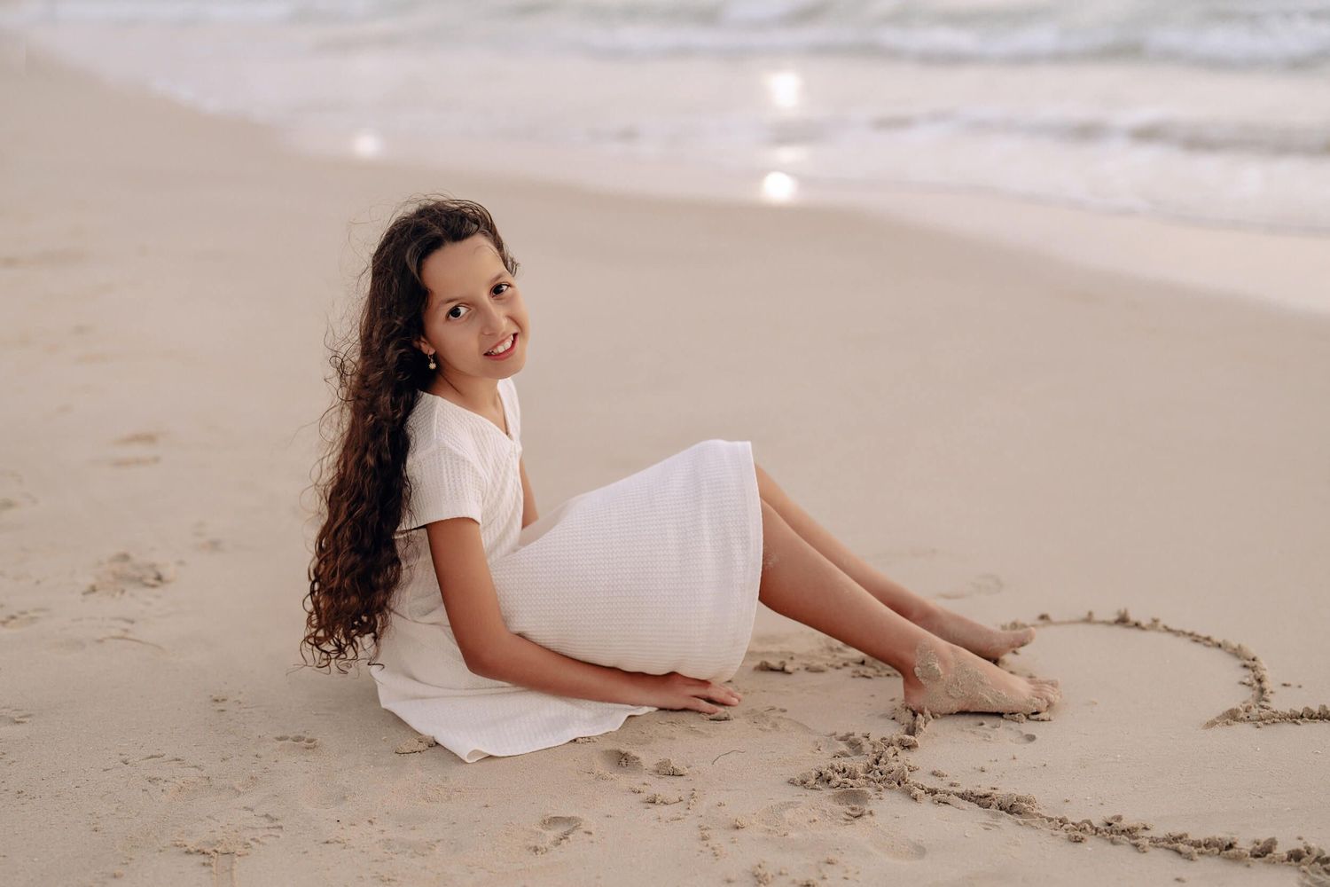 Person in white dress relaxing on sandy beach during sunset.