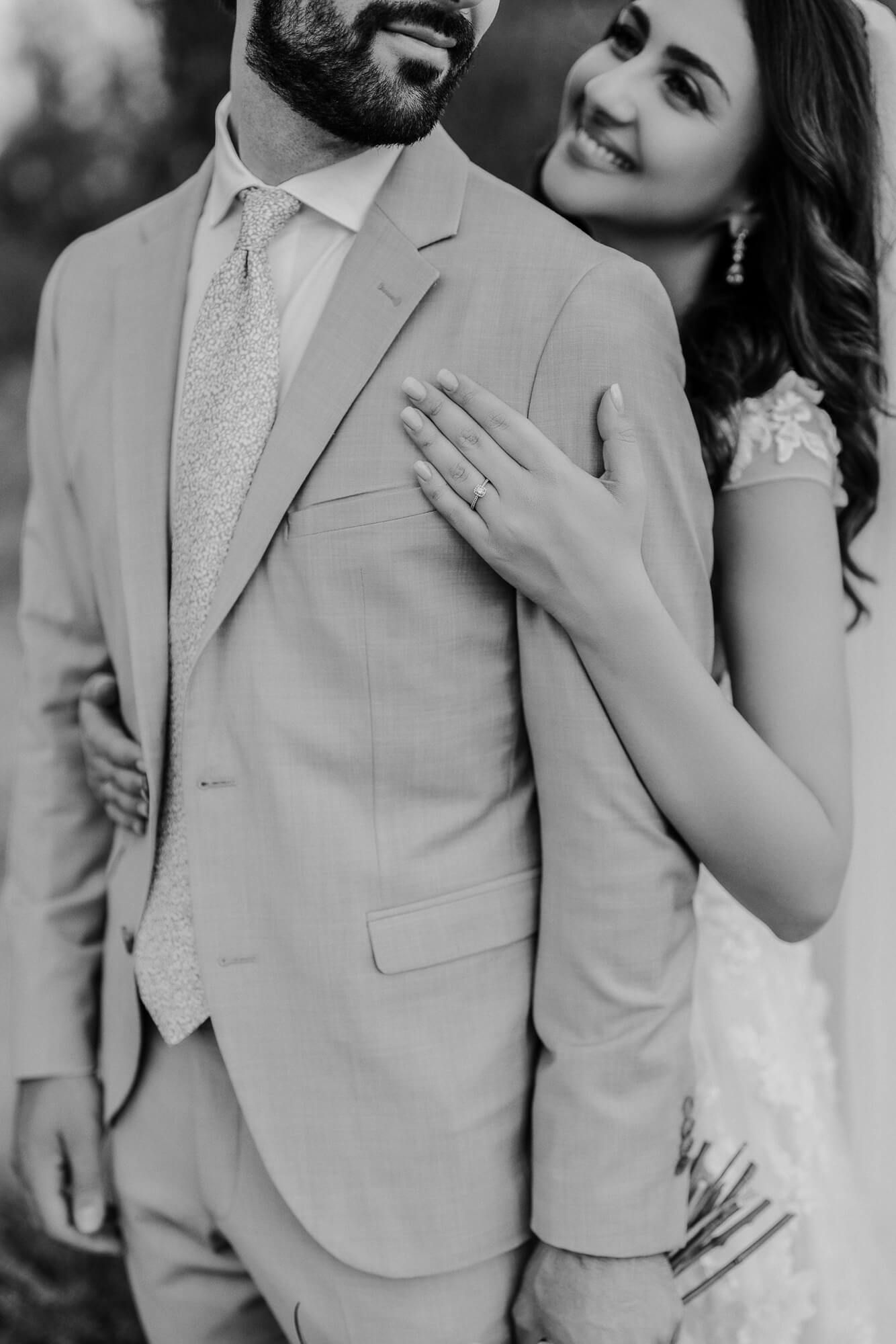 Black and white close-up photo of a couple in wedding attire showing an engagement ring and romantic embrace.