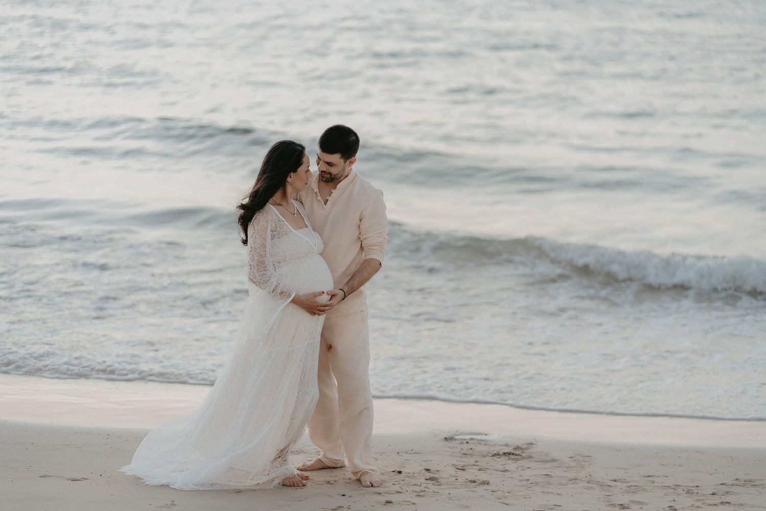 A romantic couple embraces on a serene beach at sunset, with waves gently rolling in the background.