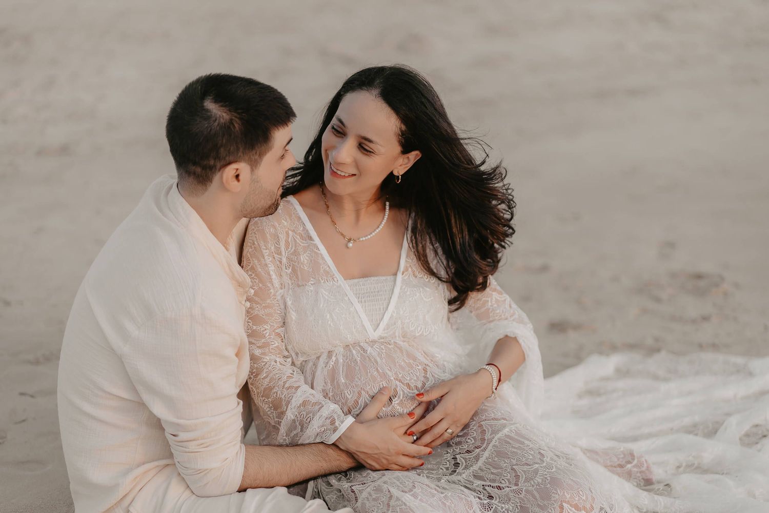 A romantic couple embraces on the beach as they share intimate moments in a black and white photo series.