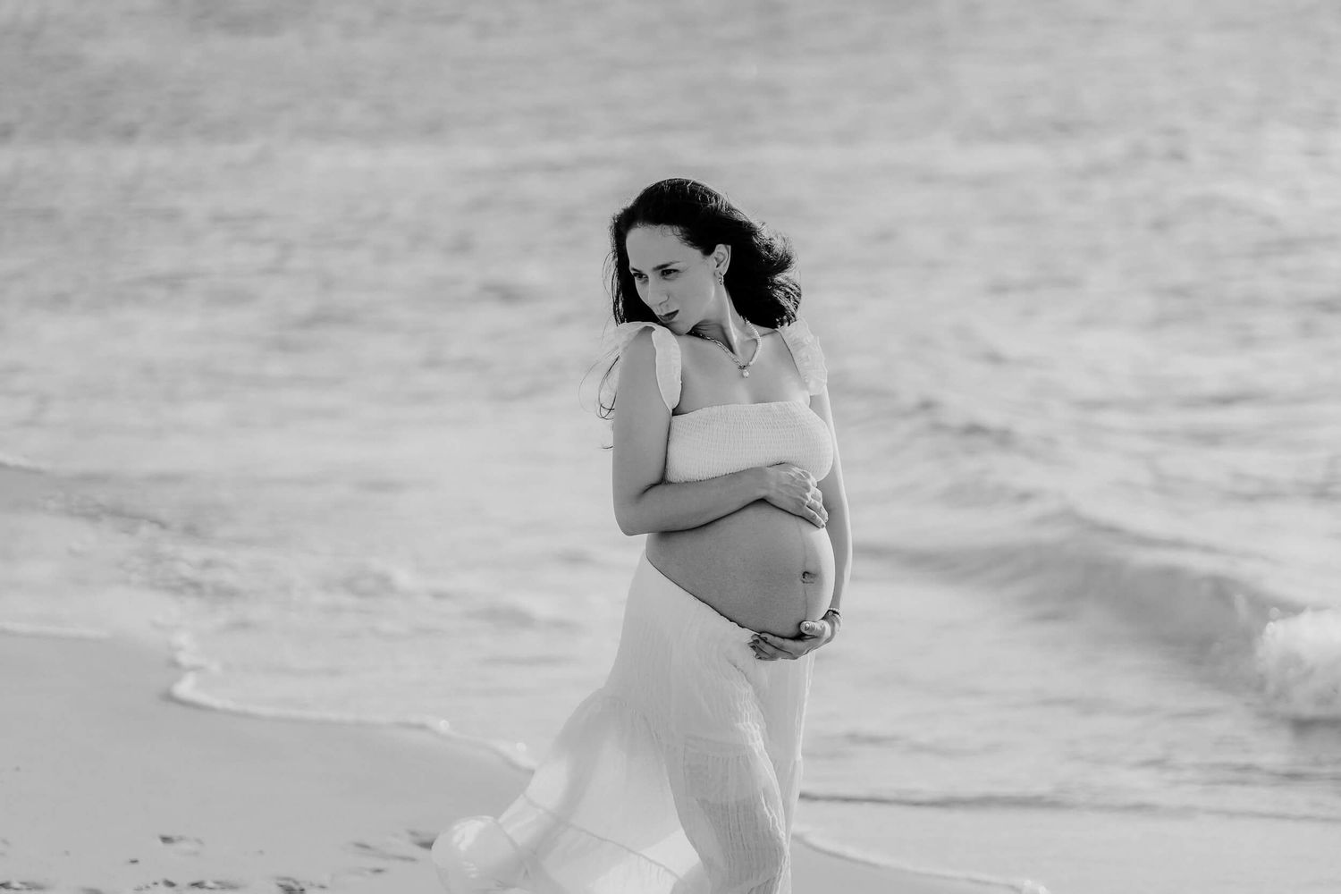 Black and white photo series of a pregnant woman in a bikini walking and posing on a sandy beach during a maternity shoot.
