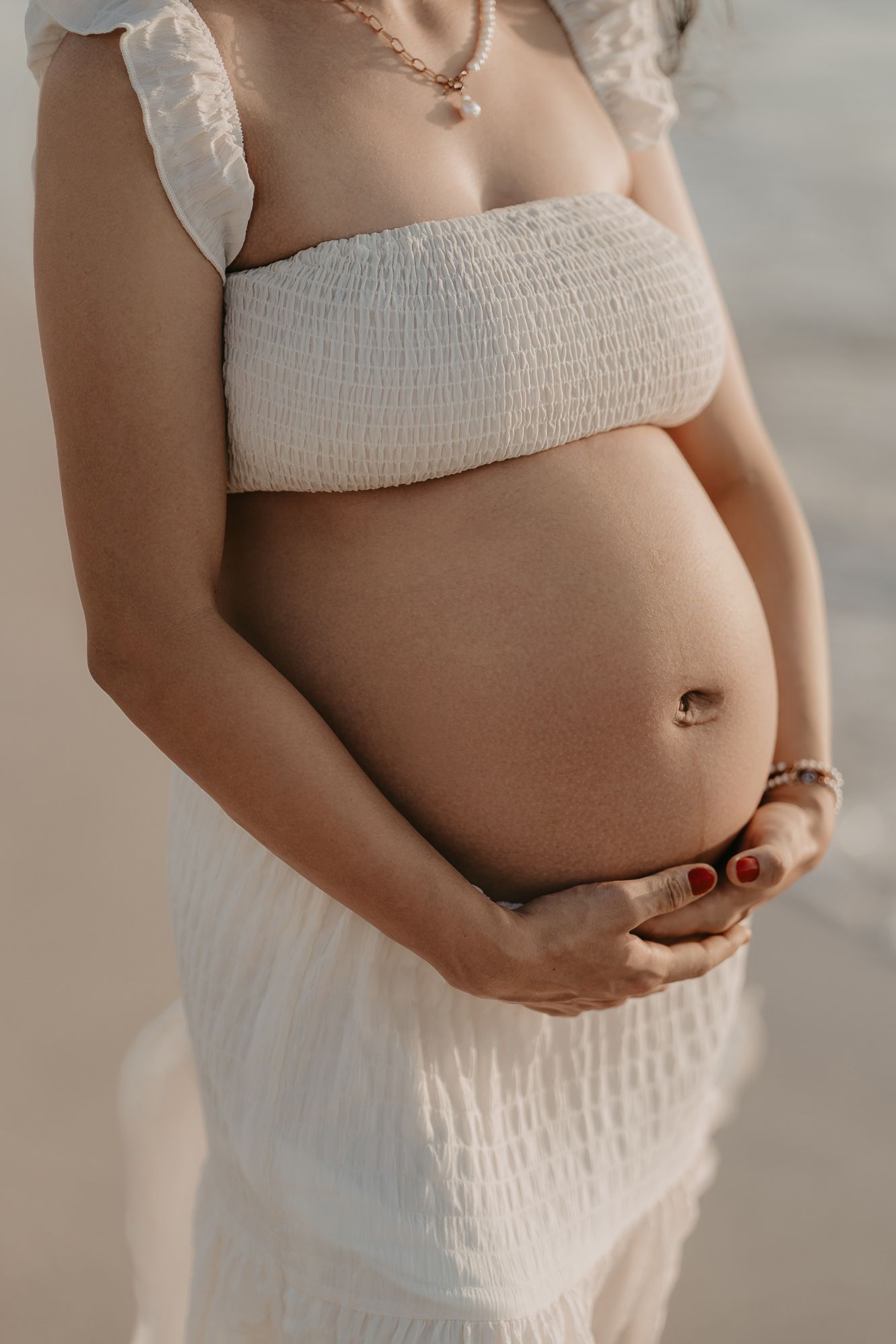 Close-up shot of pregnant belly with textured white bandeau top against soft lighting.