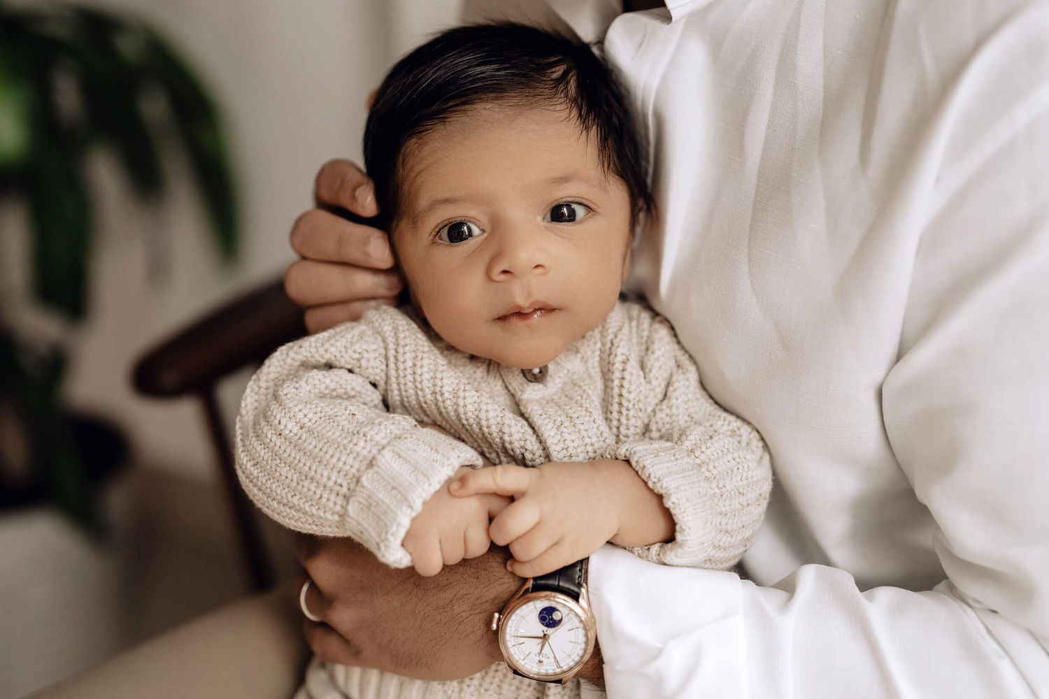 Baby in cozy sweater looking at camera while being held in parent's arms.