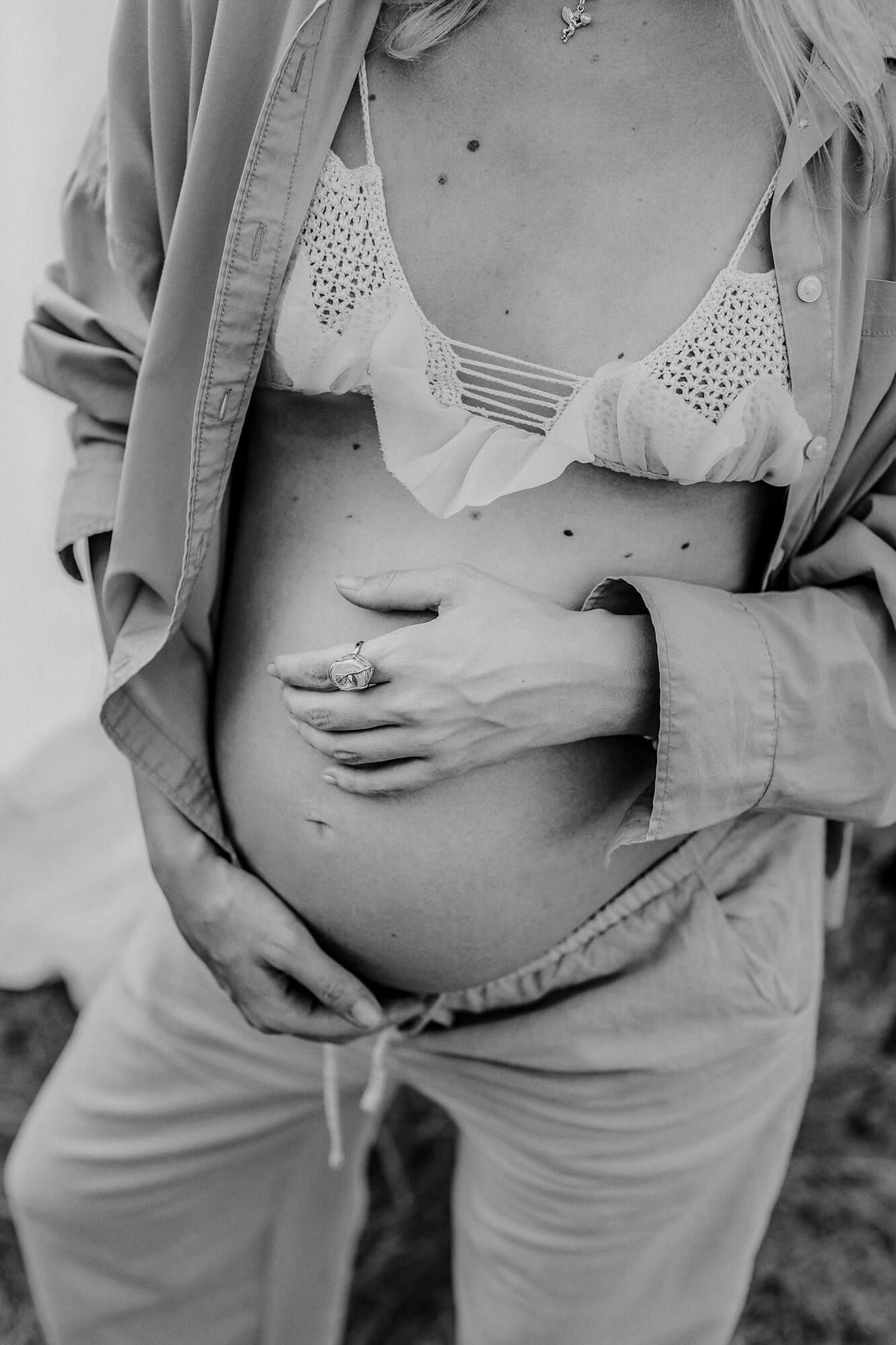 Black and white maternity photos focusing on pregnant belly with detailed clothing textures.