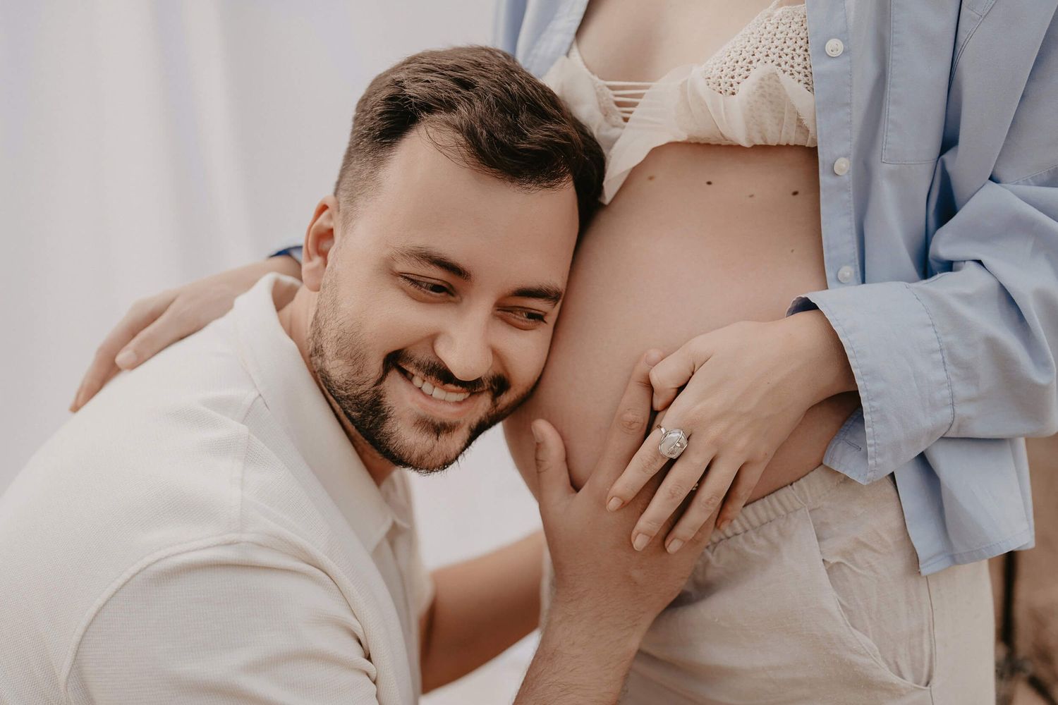 Close-up maternity photo showing joyful moment with the baby bump against white backdrop.