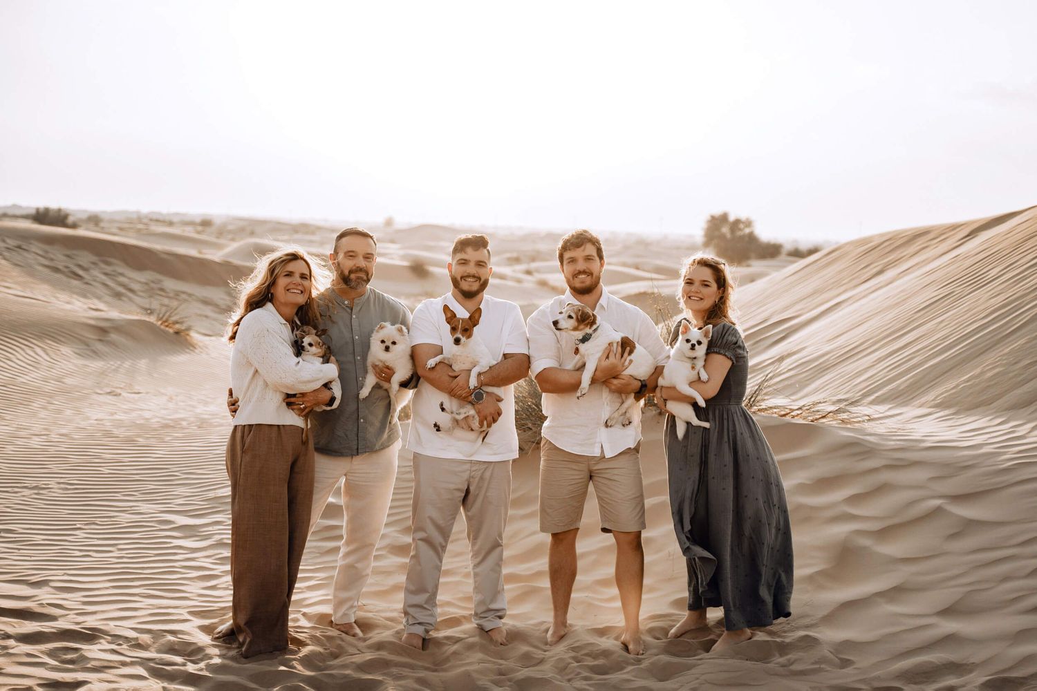 Group standing on desert sand formations holding puppies while dressed in neutral earth tones.