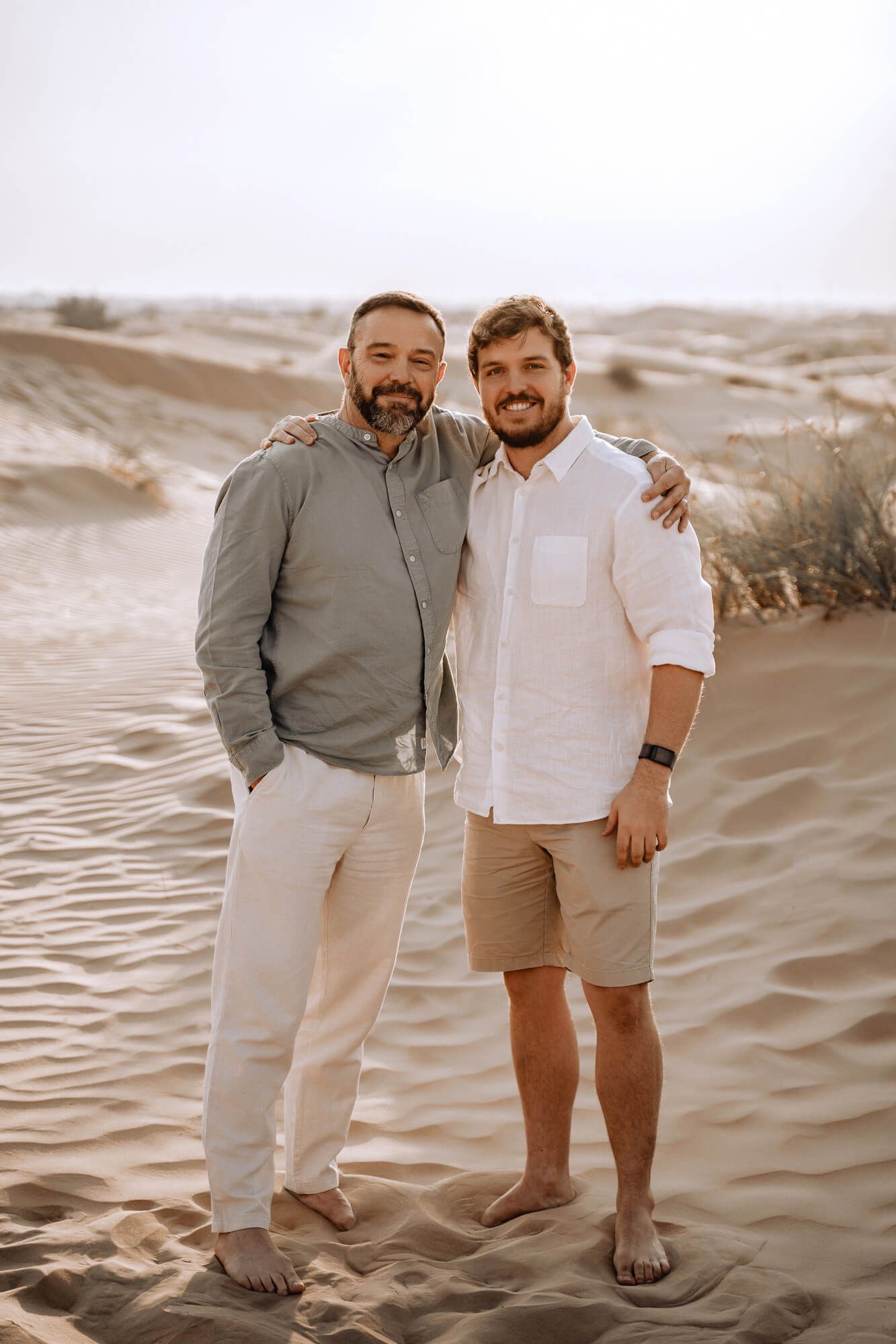 Friends stand together on sand dunes wearing complementary earth-toned casual clothing.