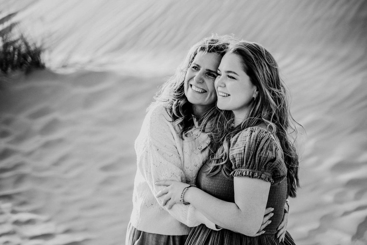 Black and white portrait of two people embracing against desert landscape.