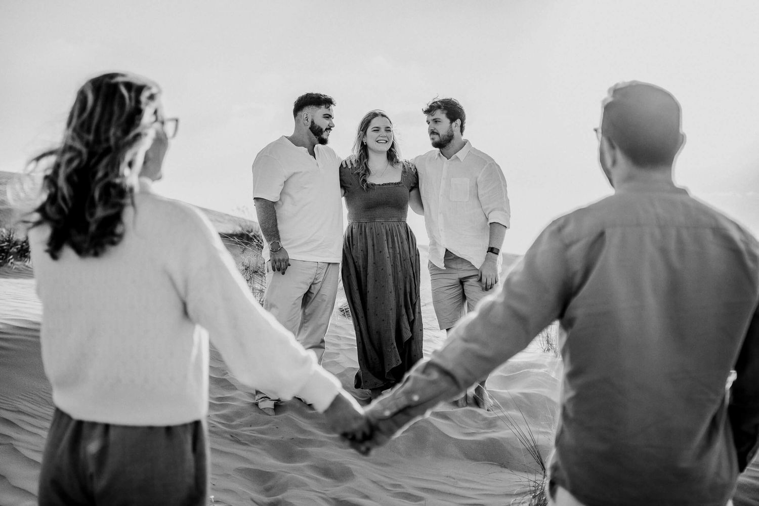 Black and white panoramic shots of group holding hands in desert setting.
