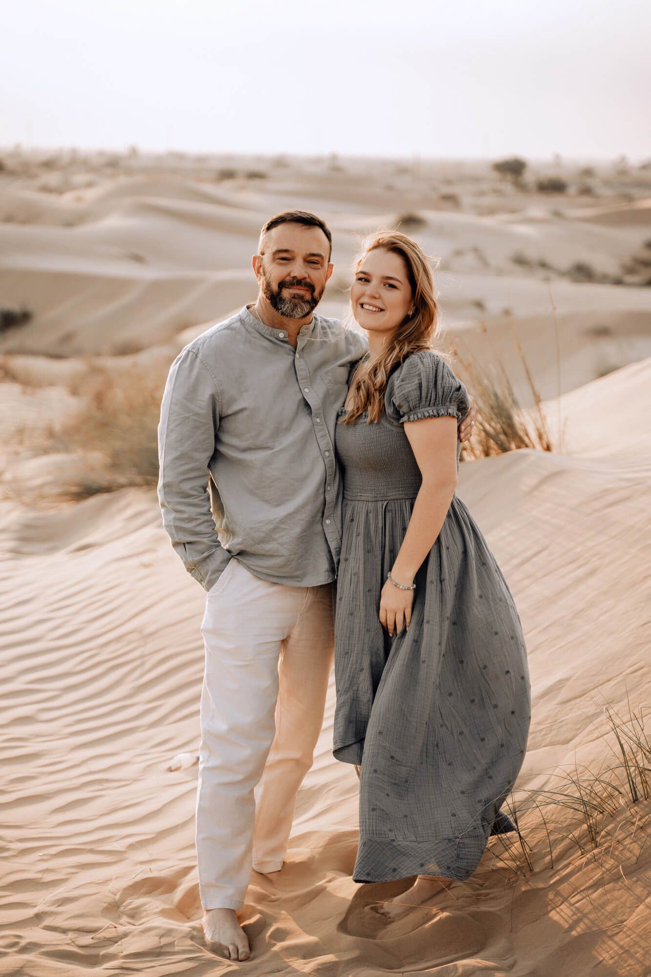Couple standing together on rippled desert sand dunes during sunset.