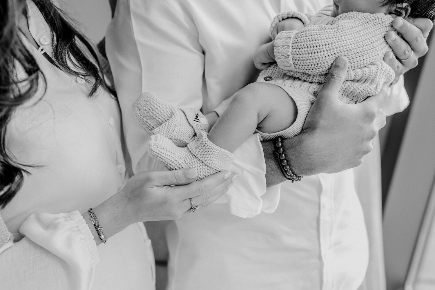 Close up of hands gently holding a tiny newborn's hands wrapped in a knitted garment.
