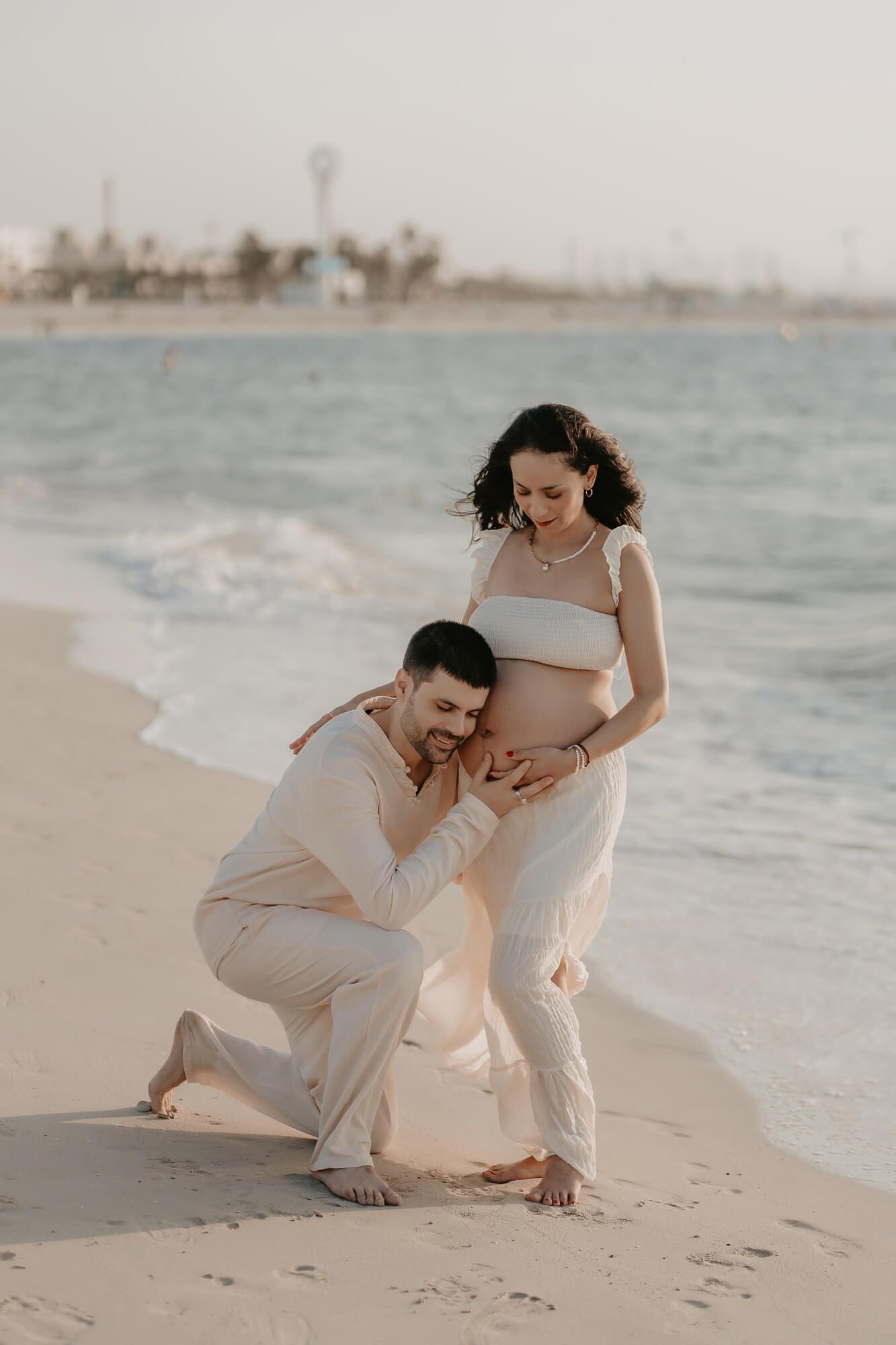 A couple shares an intimate moment on a sandy beach during sunset as they kneel together by the water.