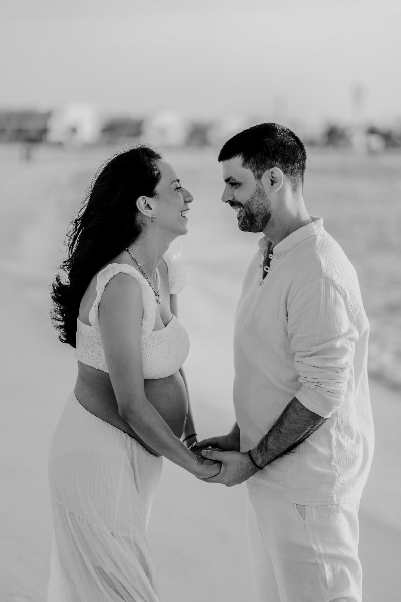 A romantic black and white portrait of a couple laughing together on their wedding day, both dressed in white.