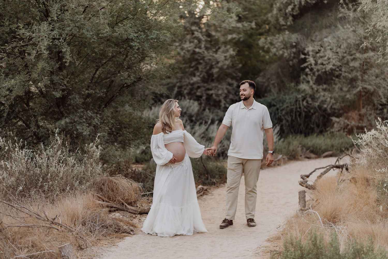 Couple walking hand in hand on a desert trail wearing white and neutral colored clothing.