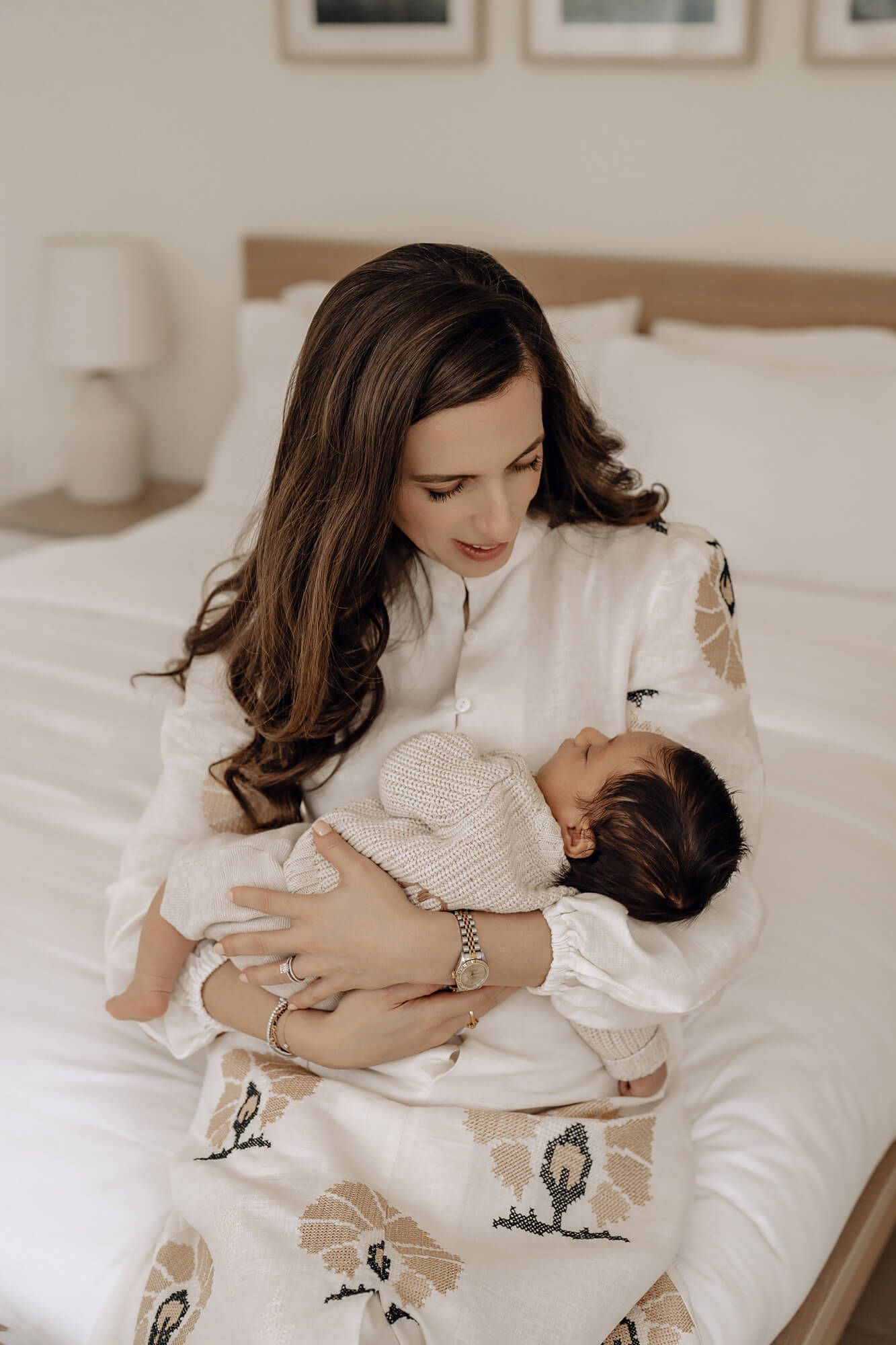 A tender moment captured in soft lighting as a parent cradles a baby in white bedding.