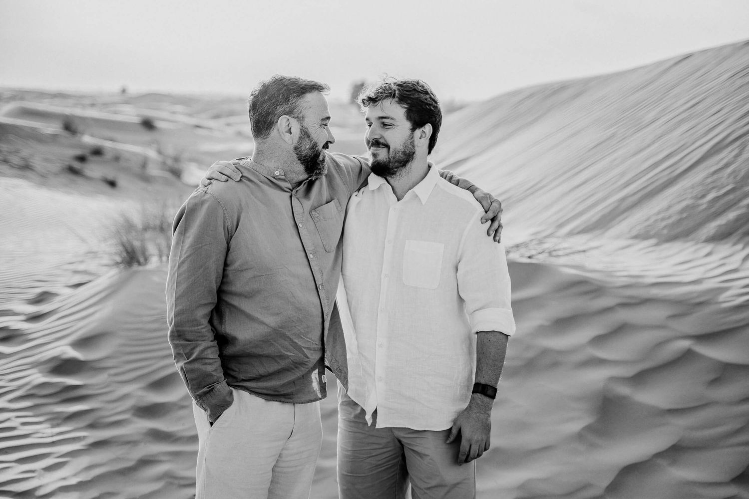 Close friends laugh together during a photo session in desert sand dunes.