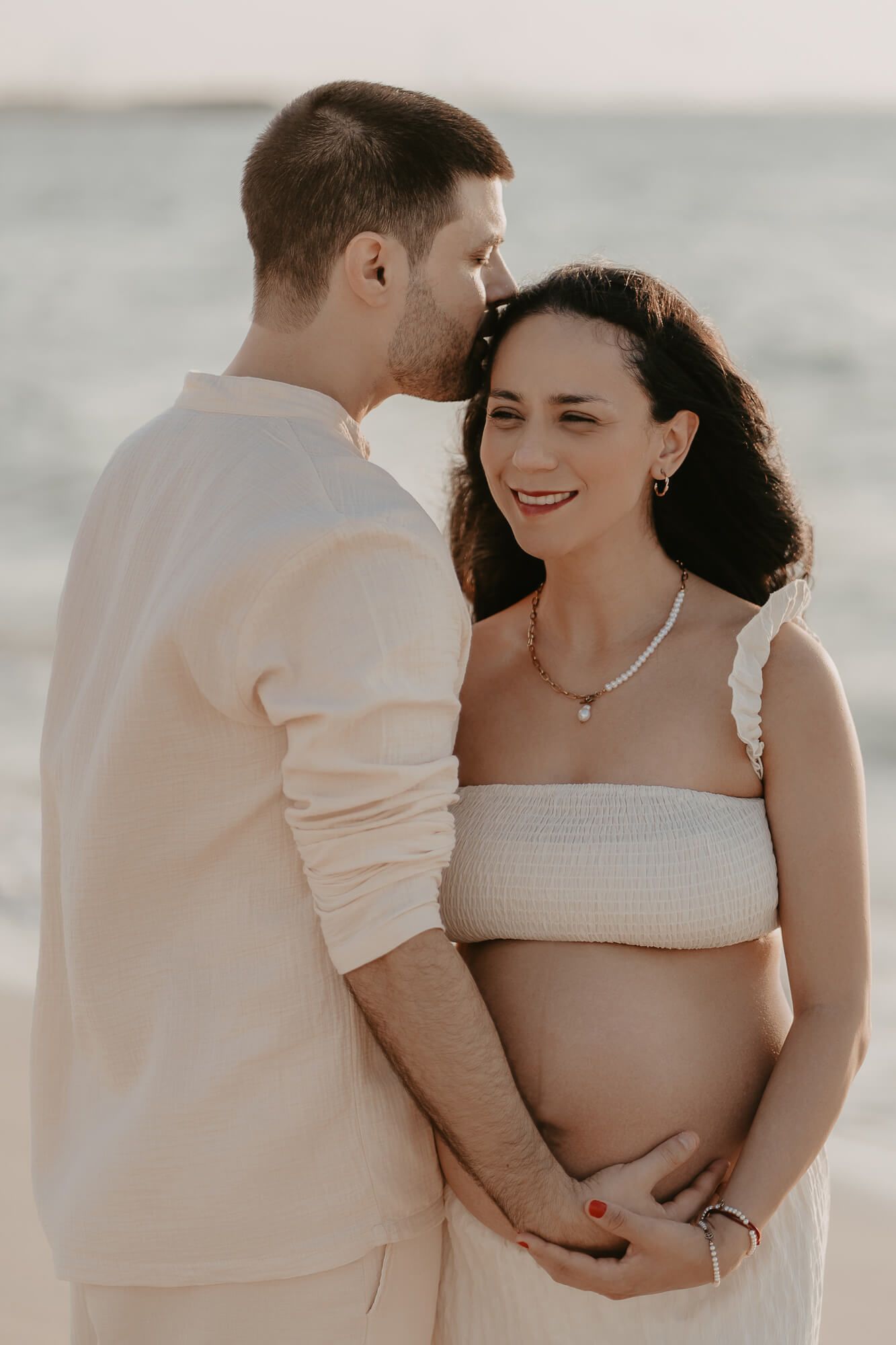 A romantic couple embraces at the beach against a soft, hazy background in neutral tones during a photo session.