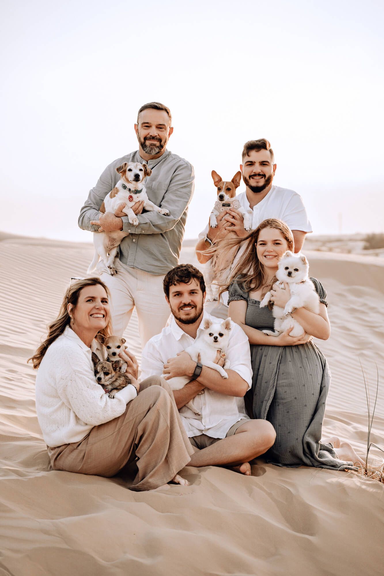 Family portrait on sand dunes with everyone holding their small dogs and smiling.