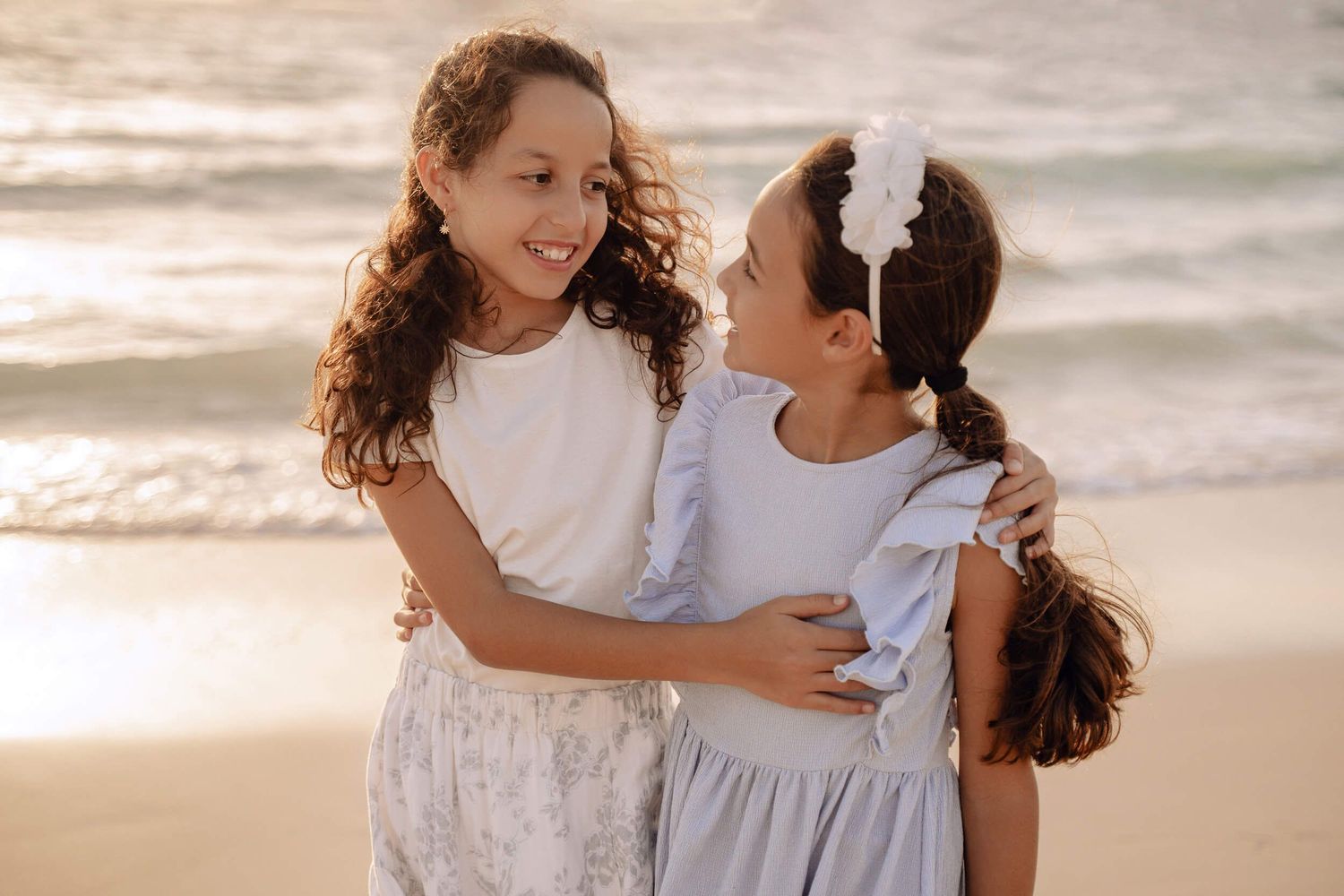 Candid beach portrait of two children sharing sisterly affection in matching dresses.