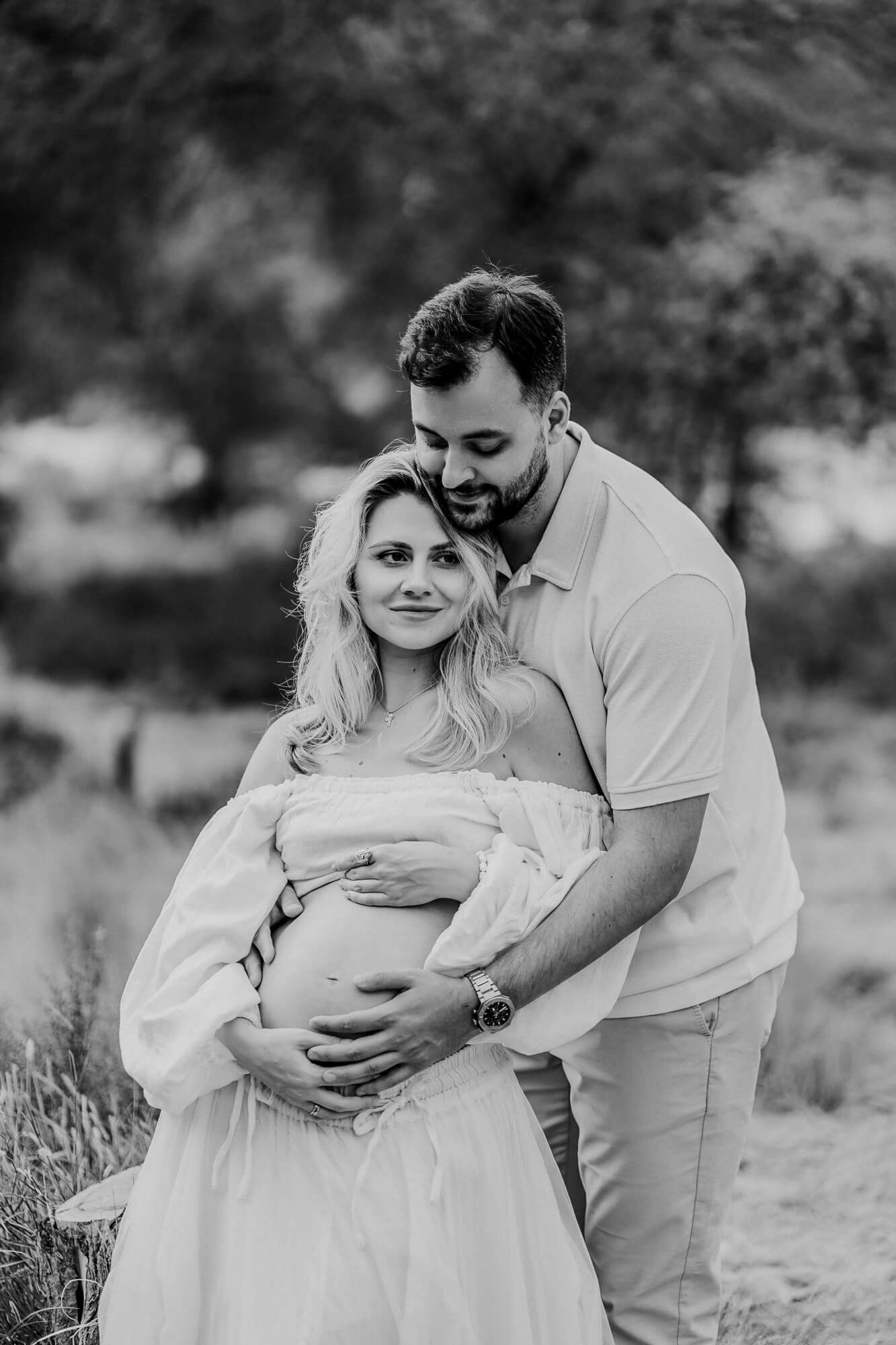 An intimate black and white maternity portrait showing loving embrace outdoors.