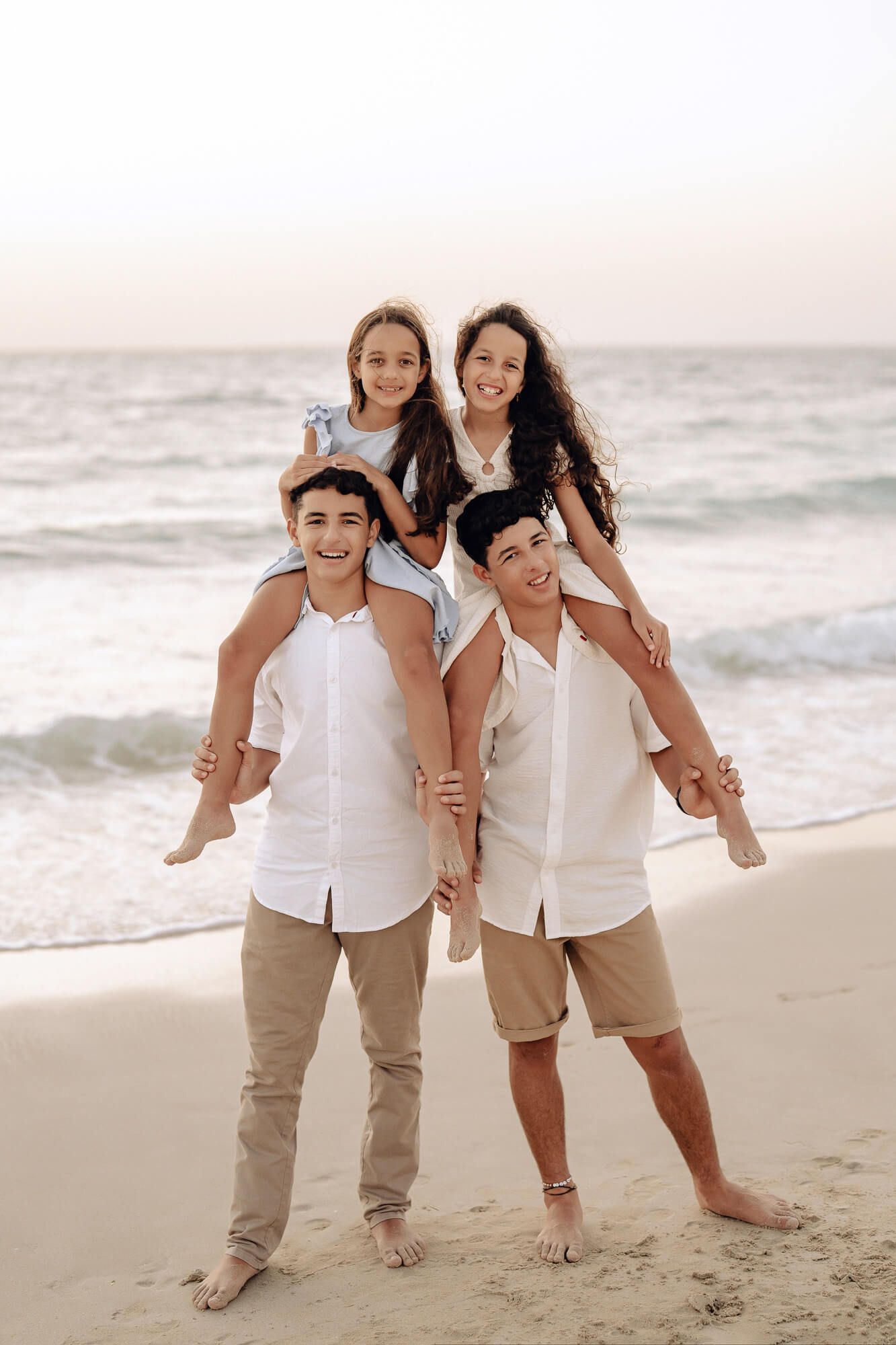 Family in coordinated white outfits posing playfully on beach at sunset.