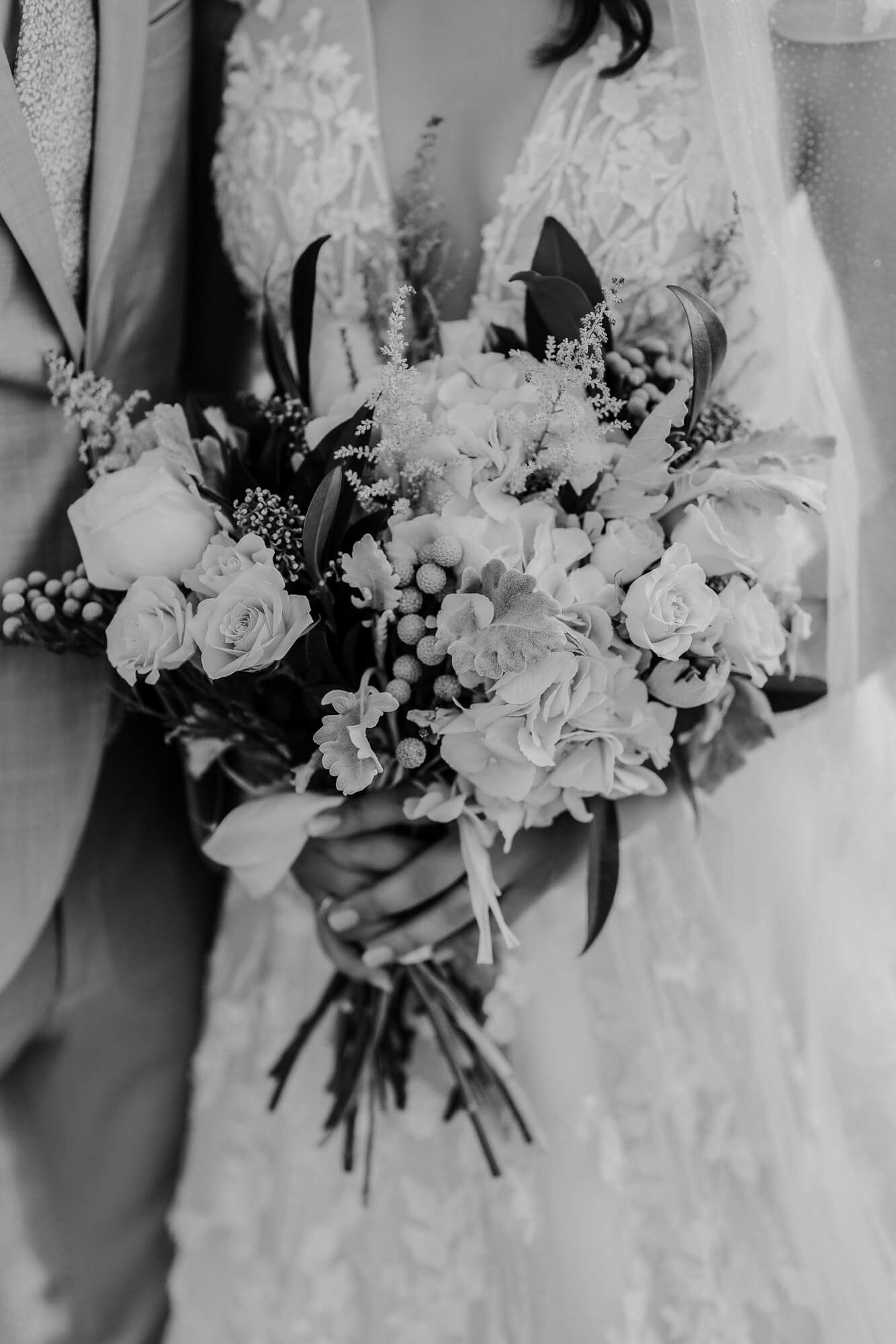 A black and white photograph of an elegant wedding bouquet featuring roses, hydrangeas and delicate foliage.