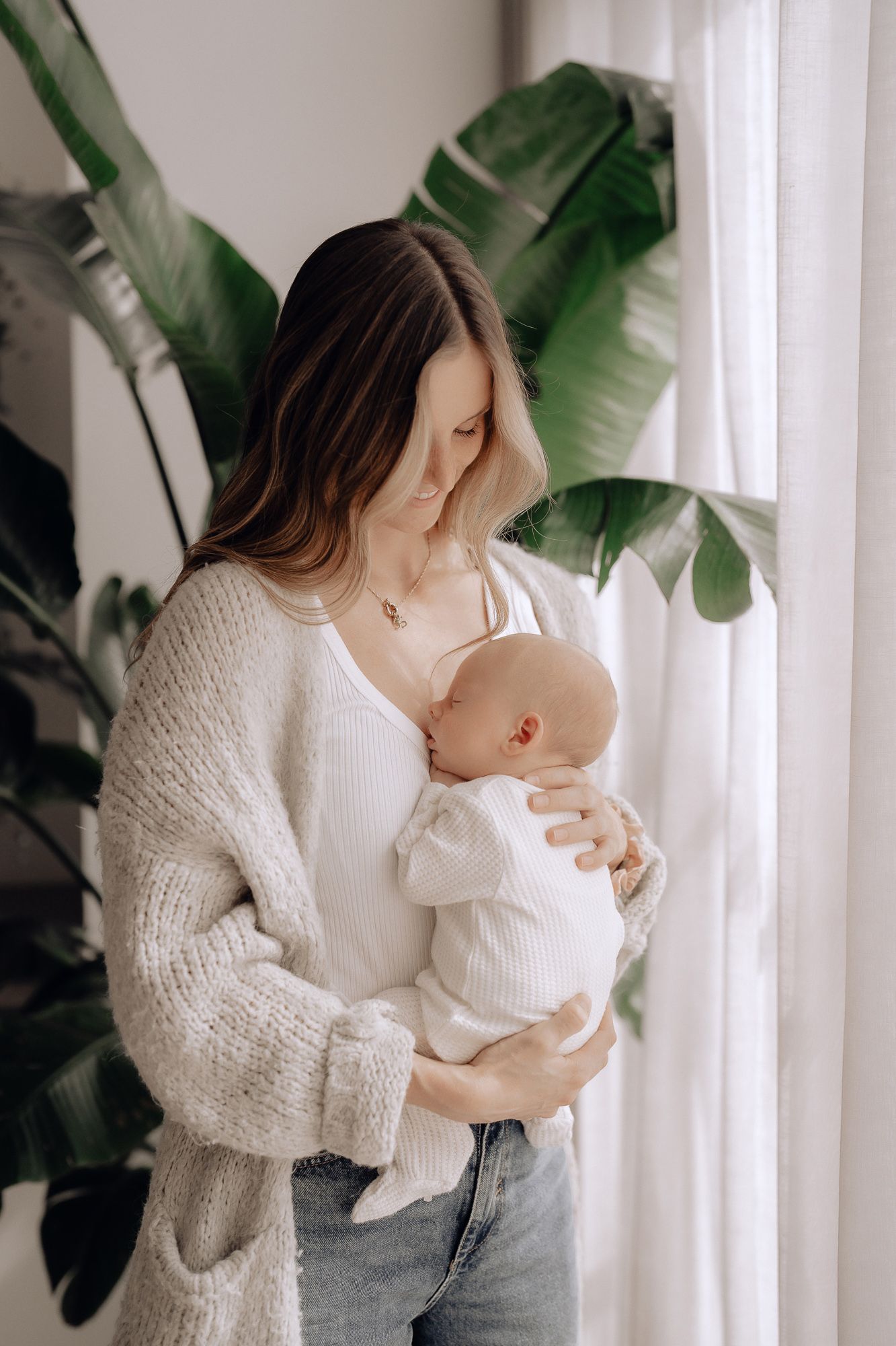 A gentle moment captured in soft light with neutral tones and potted tropical plants in the background.