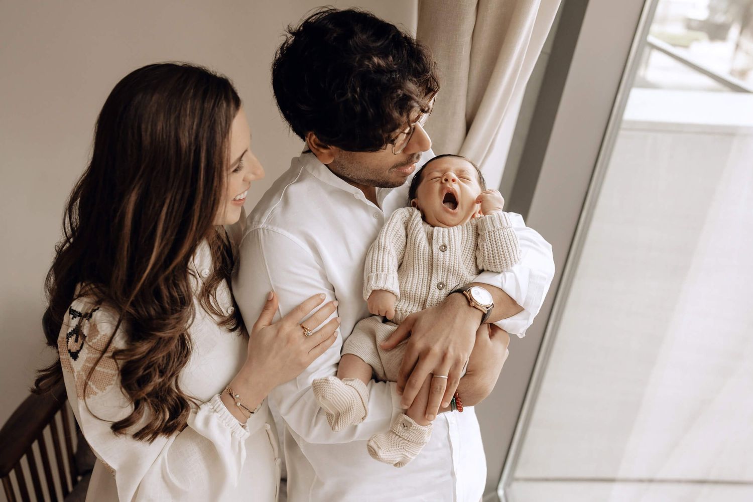 A tender indoor family lifestyle photoshoot in soft, neutral tones capturing intimate parenting moments.