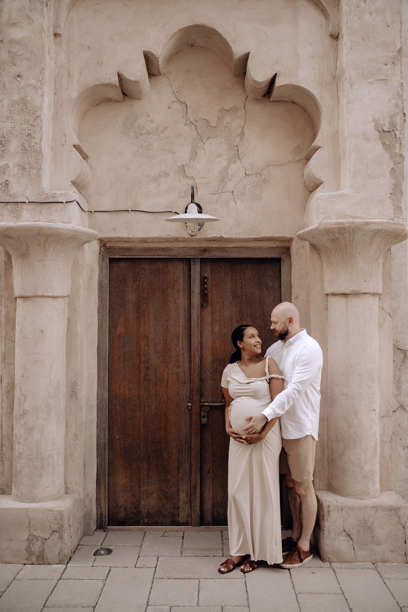 A couple shares tender moments along a stone corridor with wooden doors and arches.