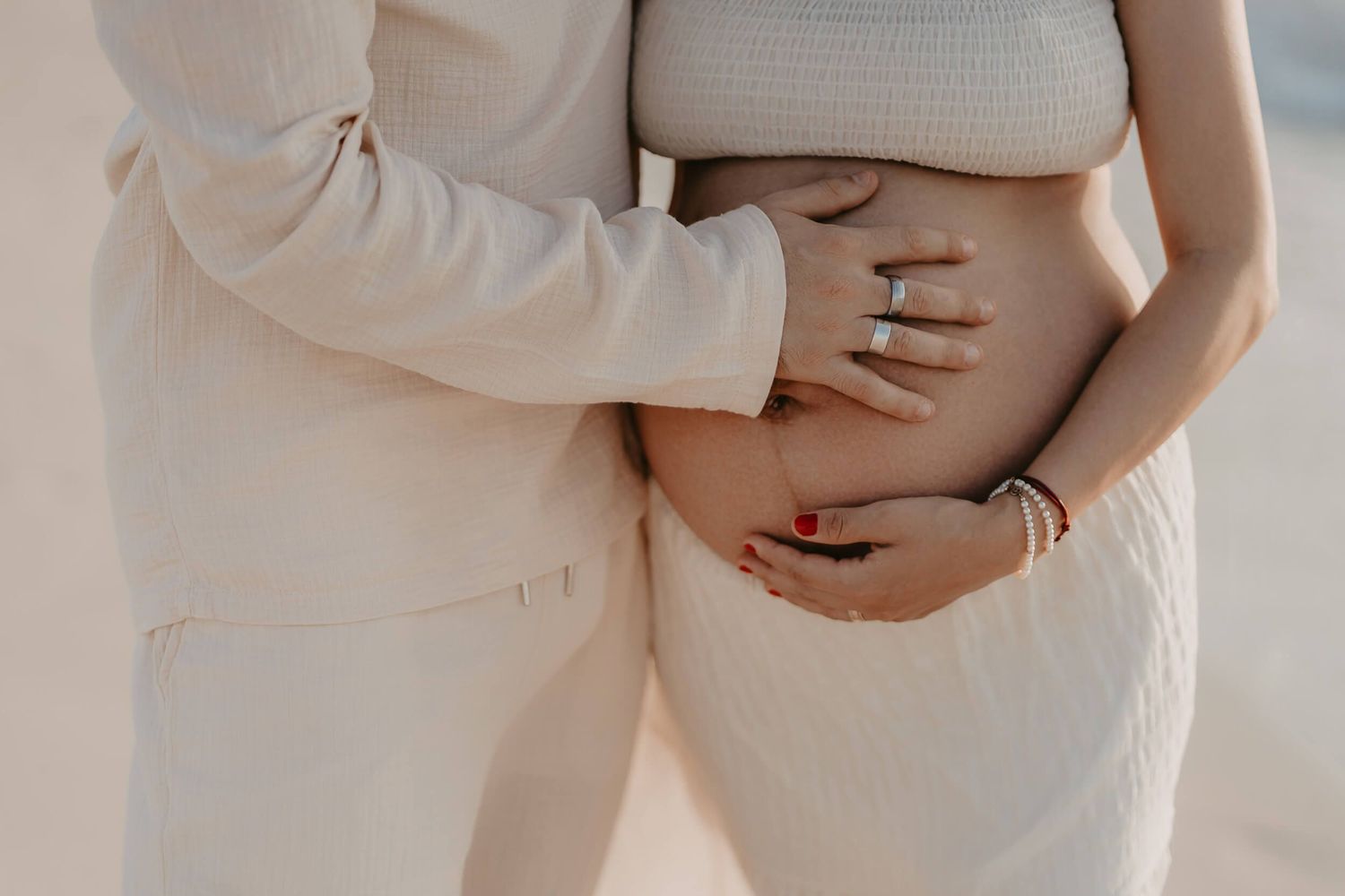 A series of side-by-side pregnancy progress photos showing a growing baby bump in cream-colored clothing against a neutral wall.