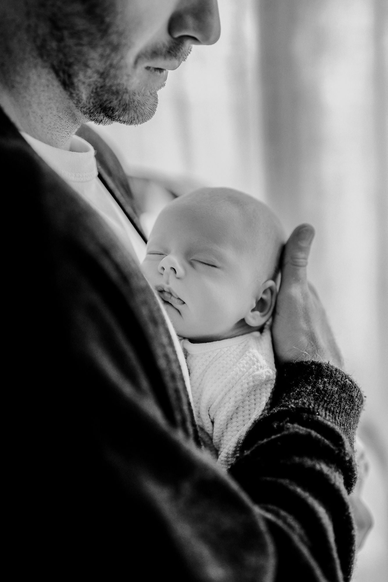 A tender black and white portrait of parent holding a sleeping newborn baby against their chest.