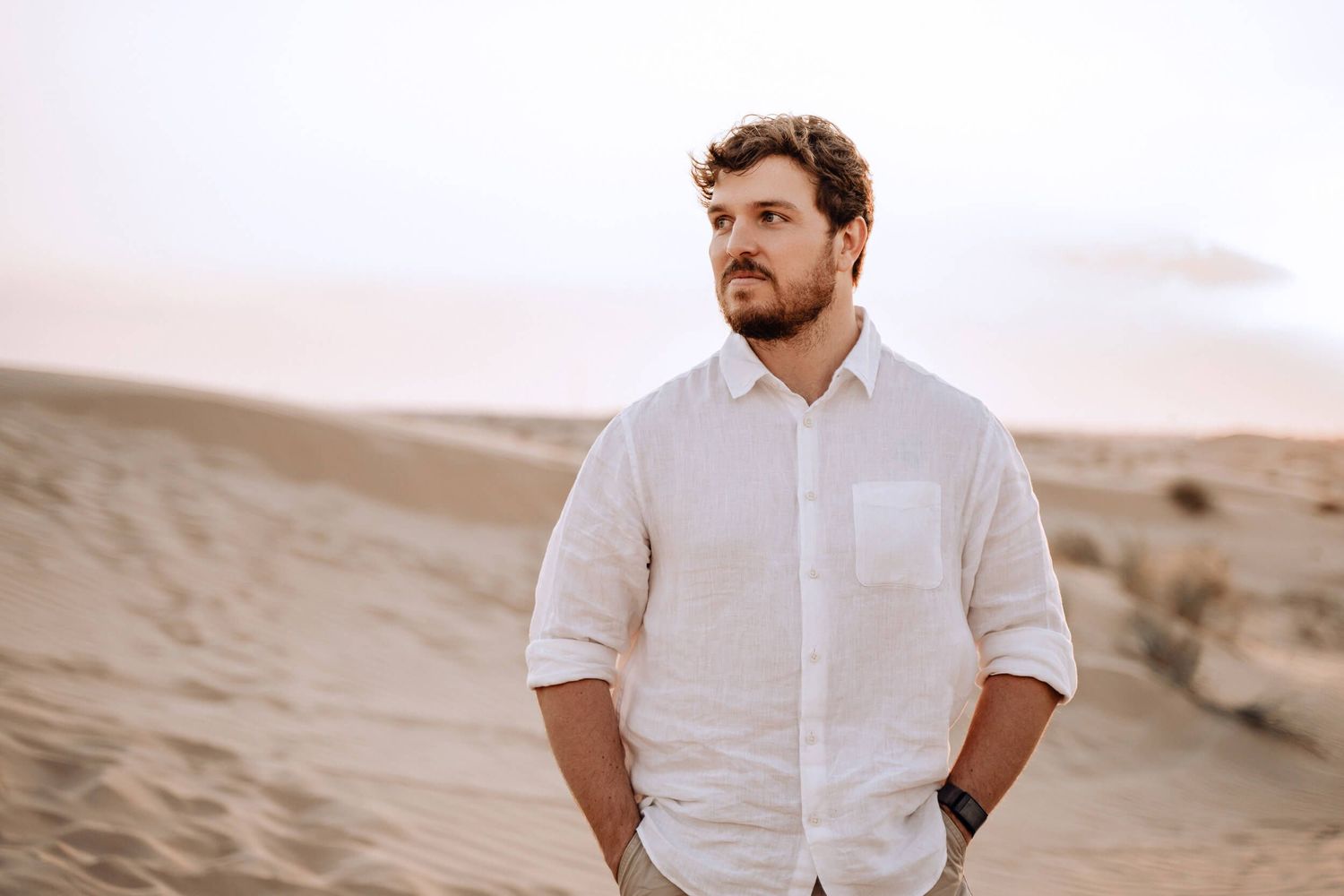 Profile portrait of person in white button-down shirt against desert landscape background.
