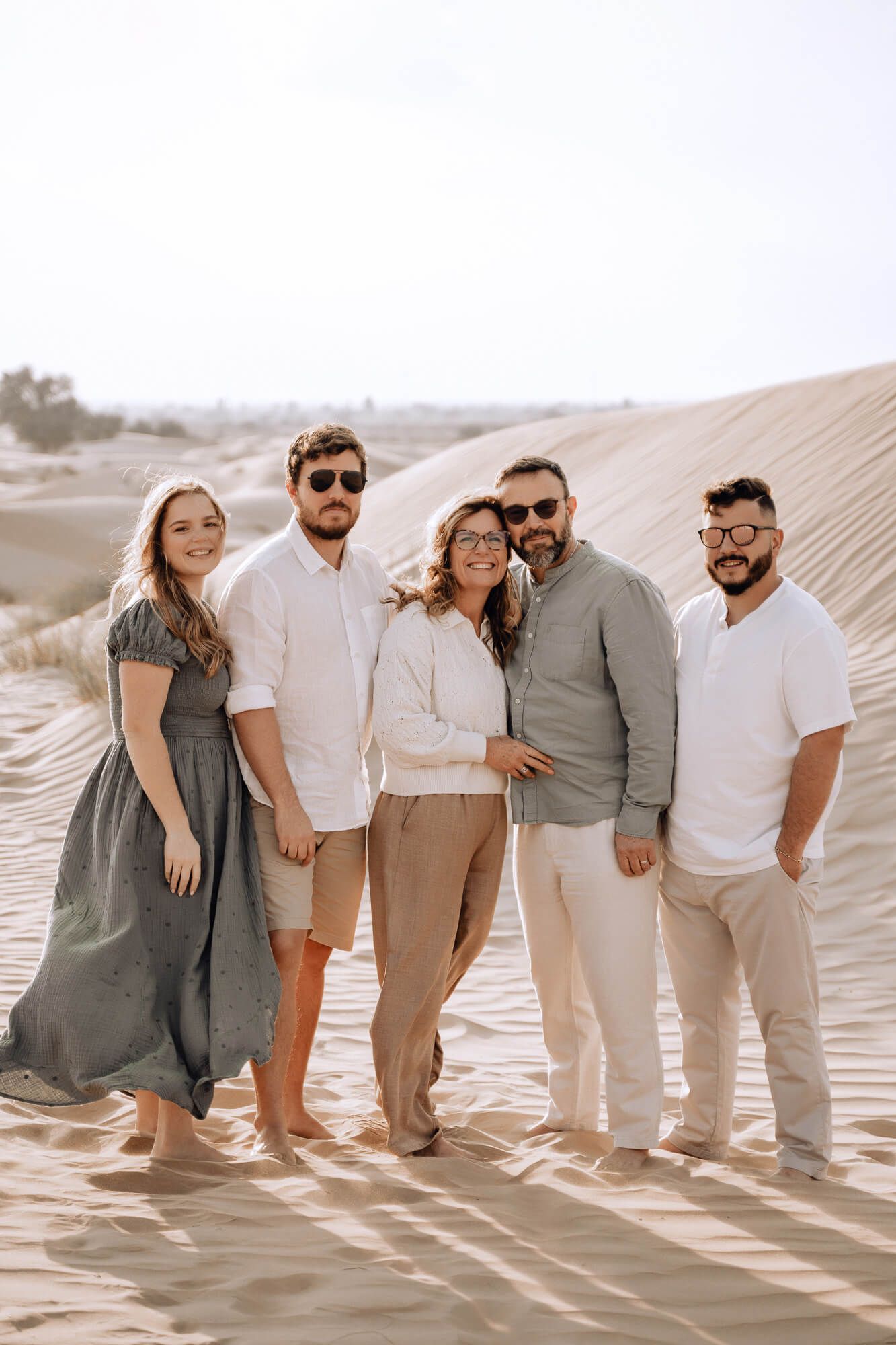 Group photo of five people in coordinated neutral outfits posing together on sandy desert dunes.