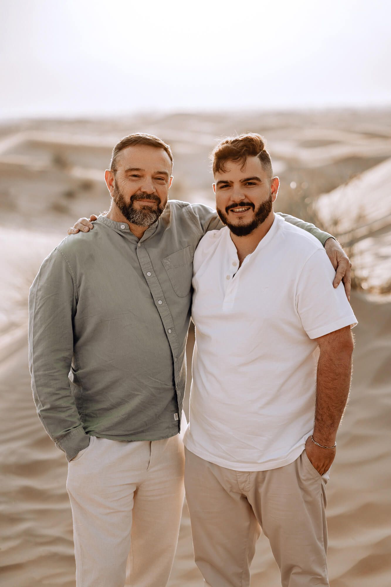 Two people in coordinating neutral outfits pose together against desert landscape.