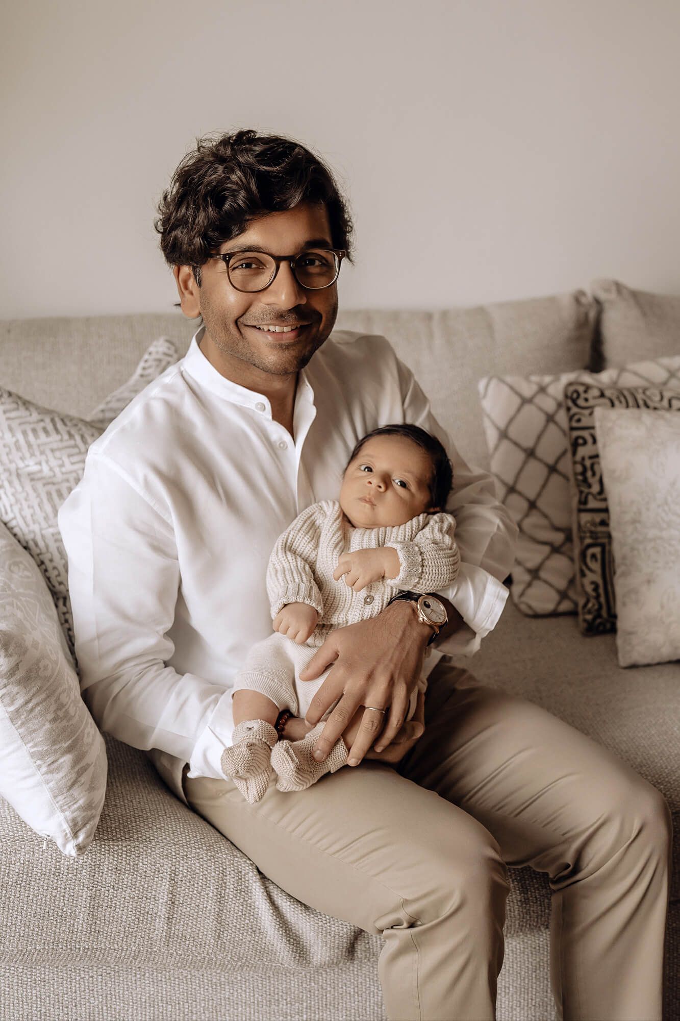 An intimate portrait on a grey couch with a baby wearing a knit sweater.