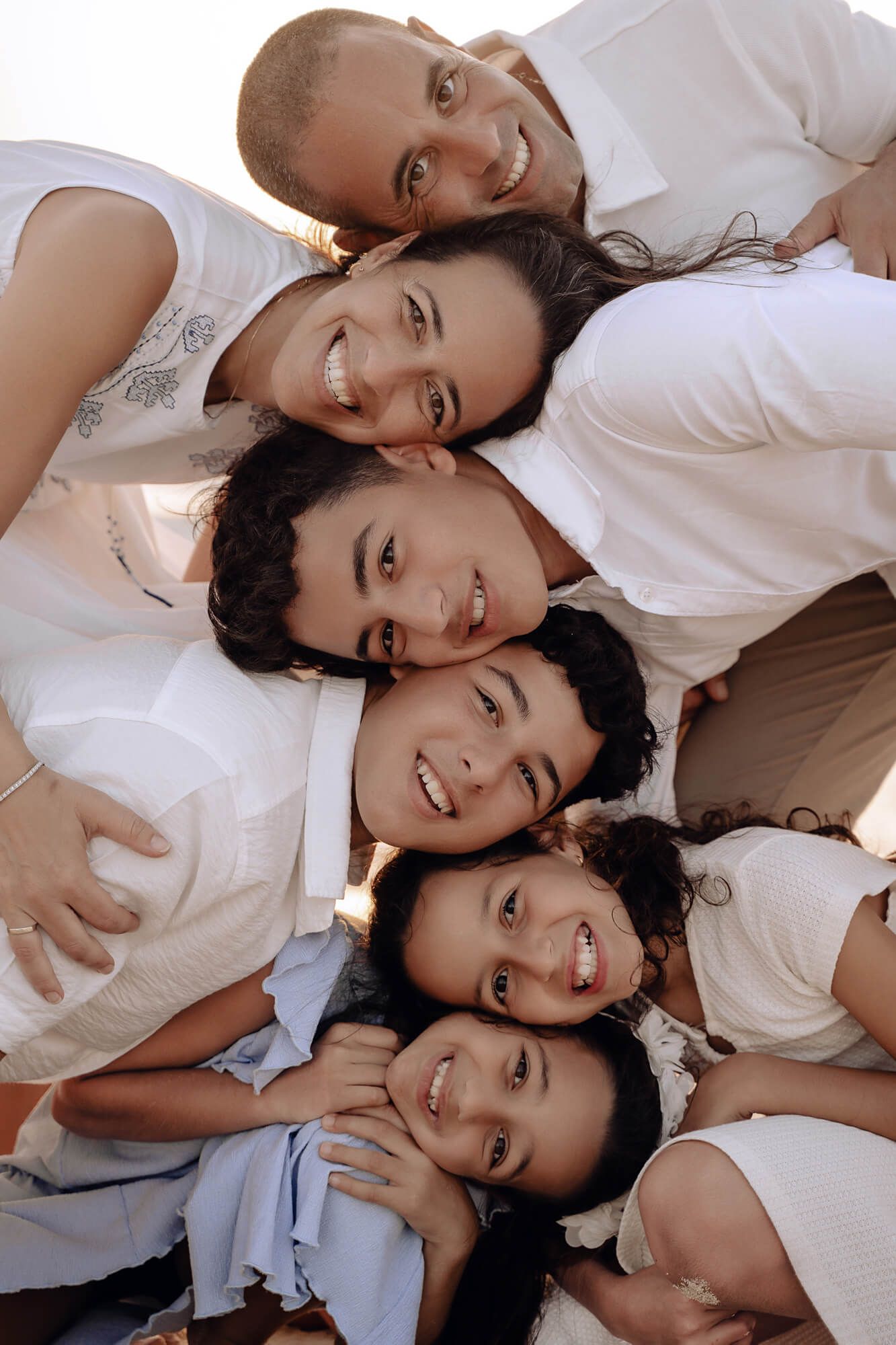 A group of people wearing white outfits huddle together in a circle formation, smiling joyfully at the camera.