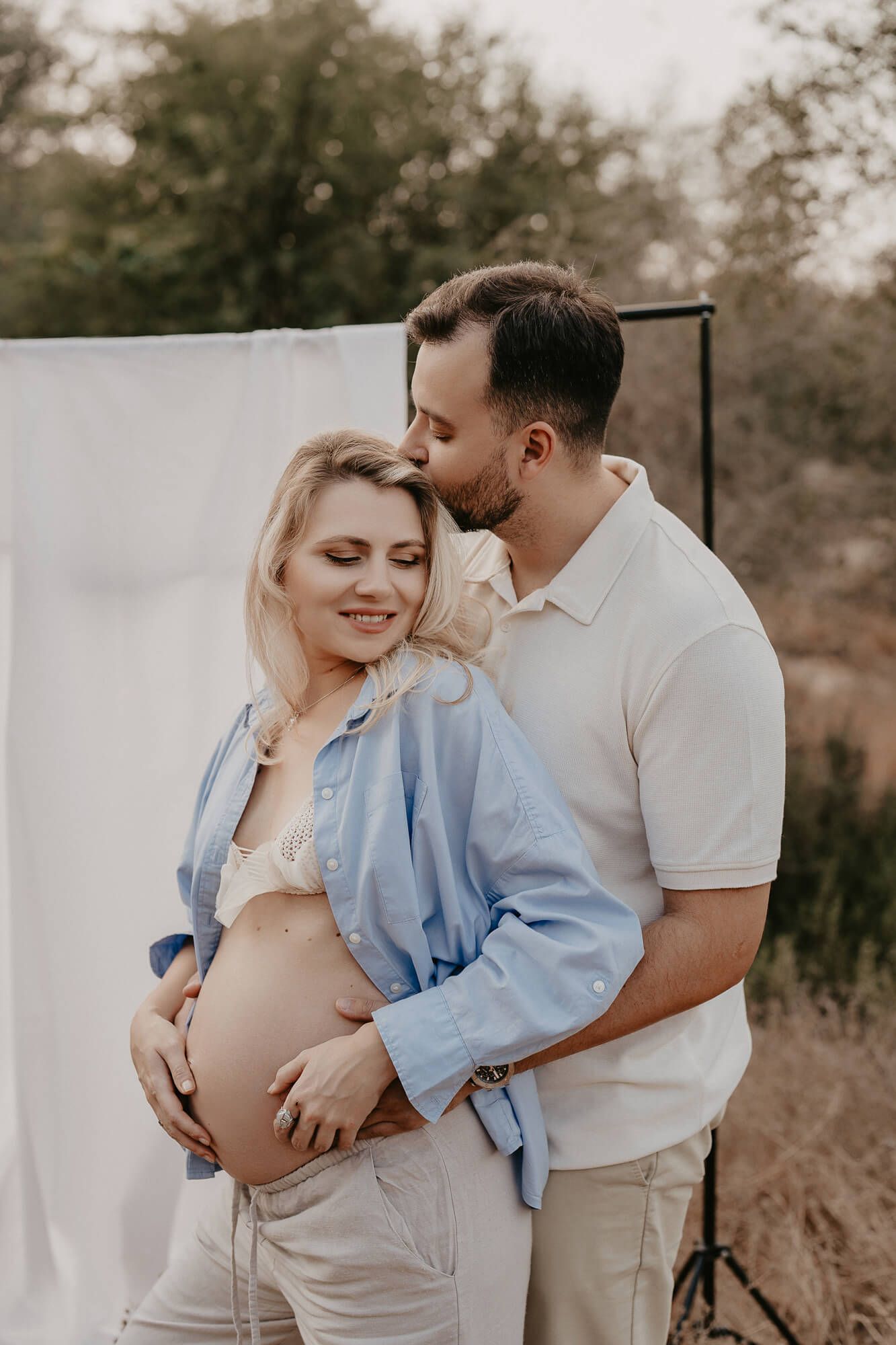 Intimate maternity photo of a couple embracing against a white backdrop outdoors.