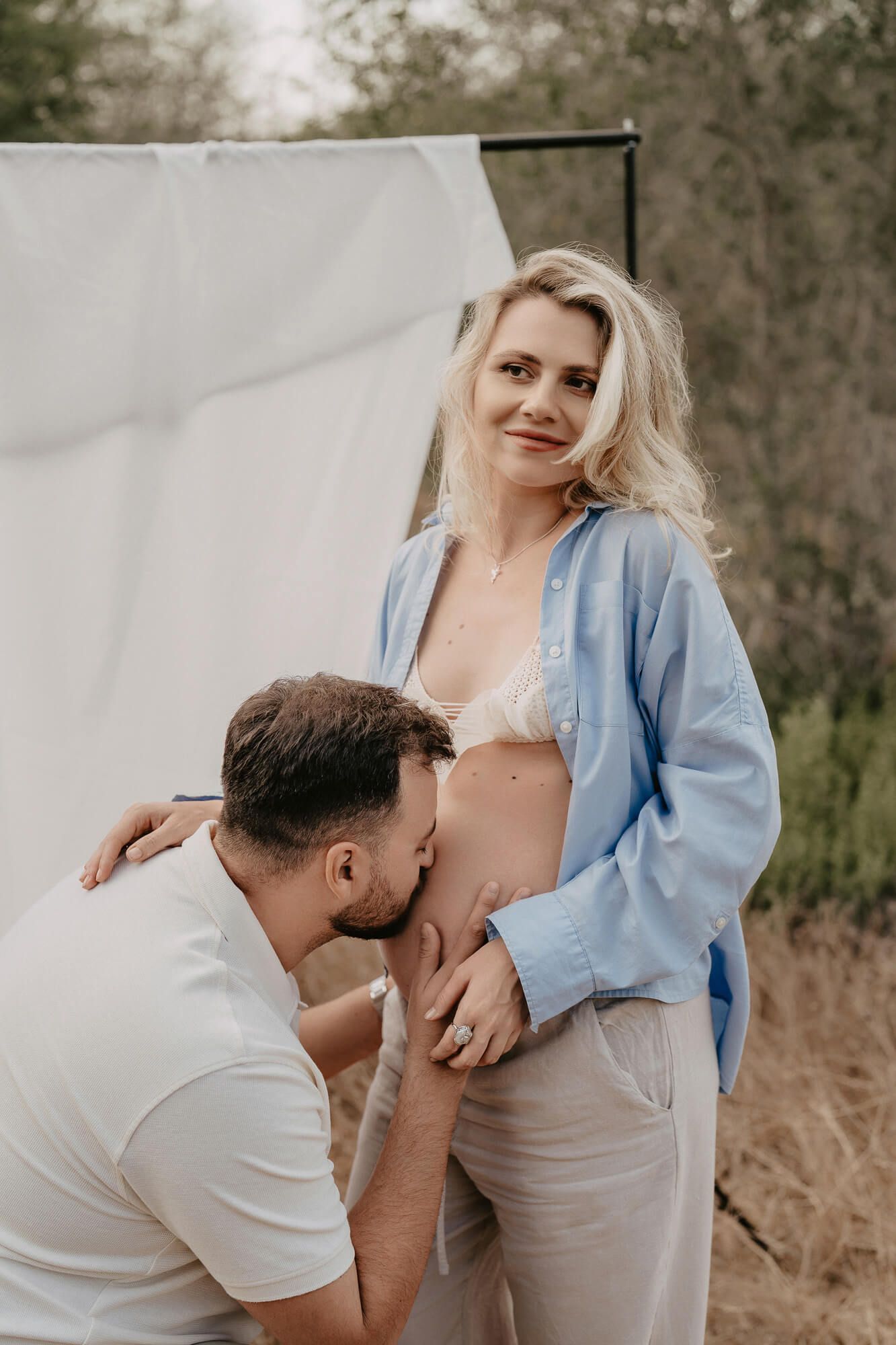 Artistic maternity portrait featuring couple in soft natural lighting against neutral backdrop.