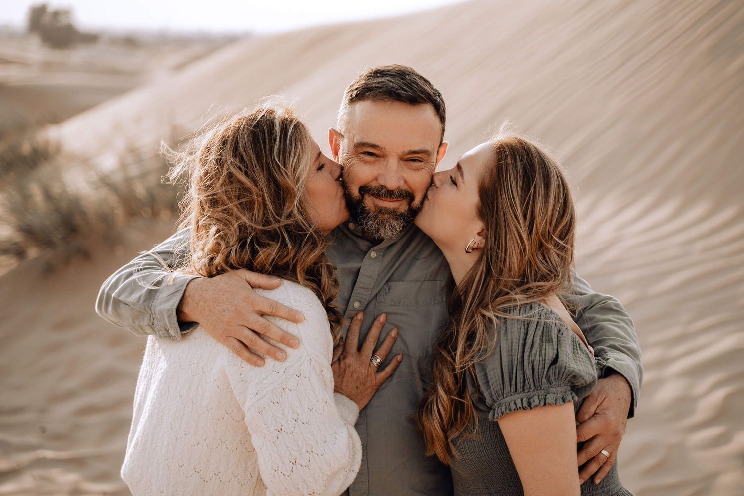 Candid moment of affection between three people embracing against a desert landscape backdrop.