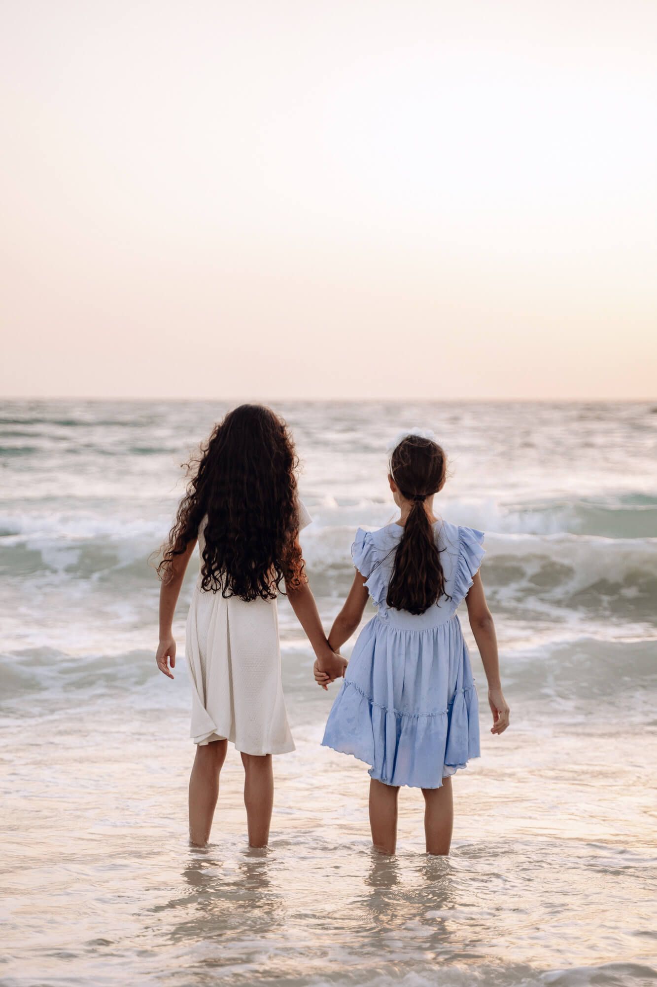 Two figures wade into gentle ocean waves during a dreamy sunset.
